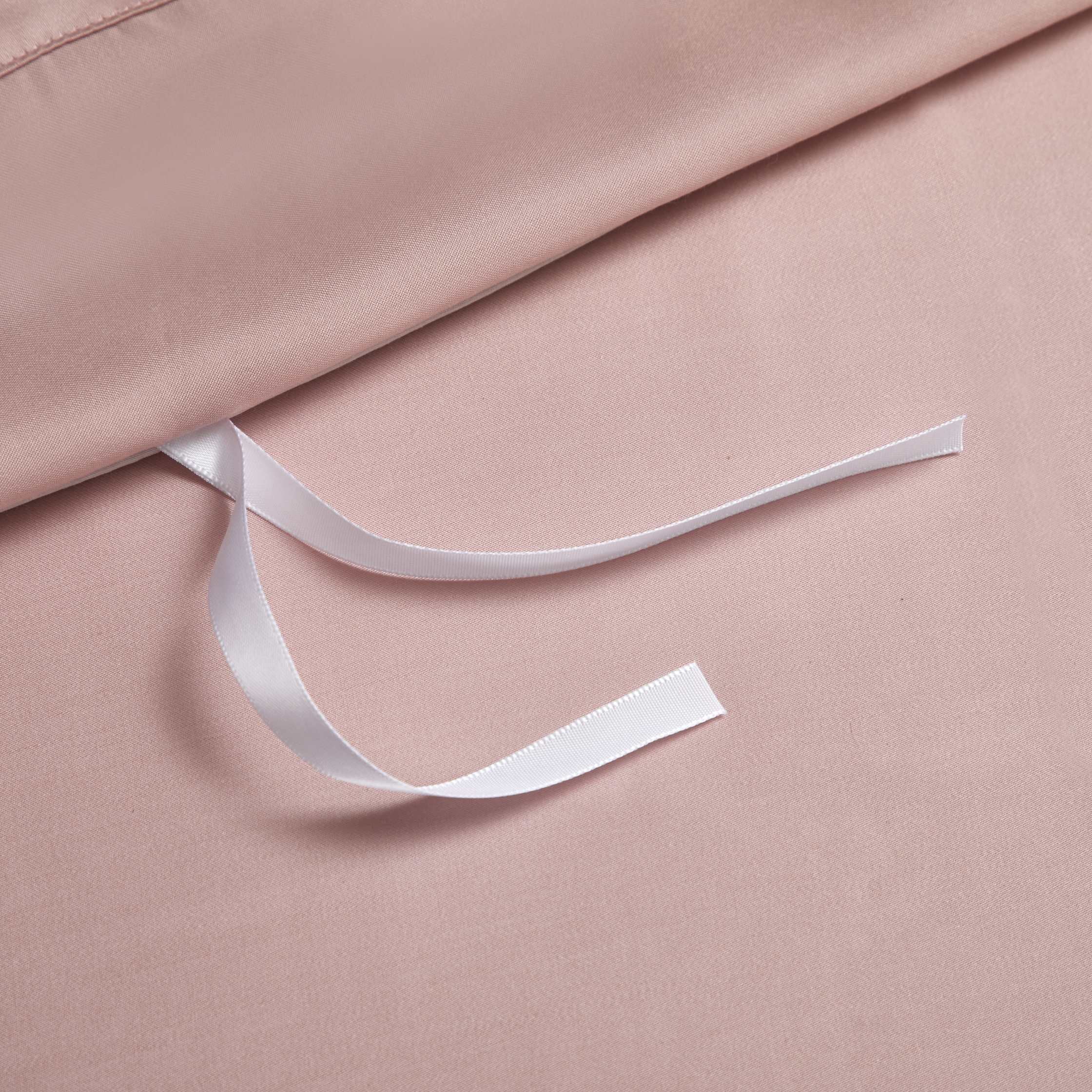 A close-up of a blush pink silk duvet cover featuring an internal white ribbon tie for securing the duvet. The smooth, lustrous fabric highlights its premium quality, while the ribbon provides a functional detail for maintaining duvet placement.