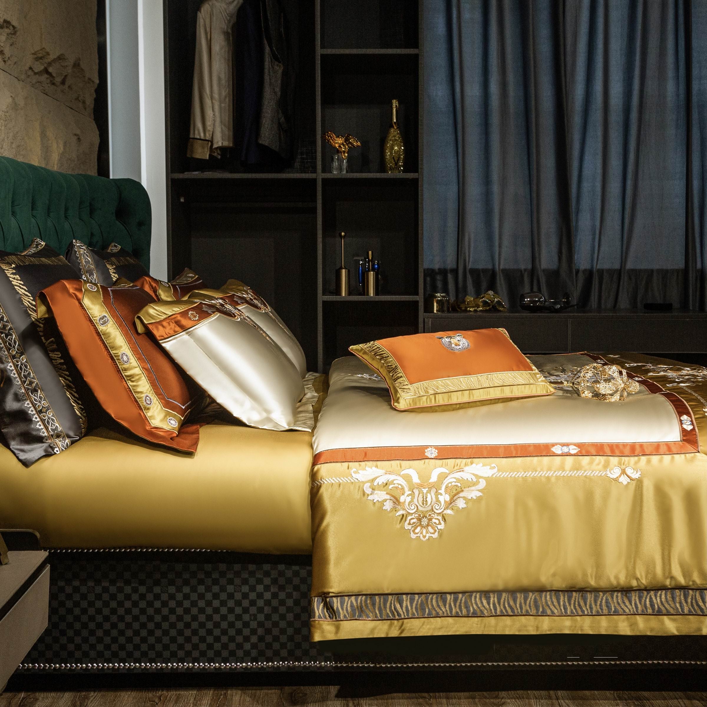 A side view of an exquisite bedding setup, featuring a luxurious gold and ivory satin duvet cover with intricate embroidery in baroque-inspired patterns. The set includes elegant pillowcases in complementary shades of black, ivory, and orange, each adorned with detailed embellishments and metallic trims. A decorative orange pillow with gold accents takes center stage, enhancing the grandeur of the arrangement. The bed is set against a dark green tufted headboard, and a chic wardrobe in the background adds a