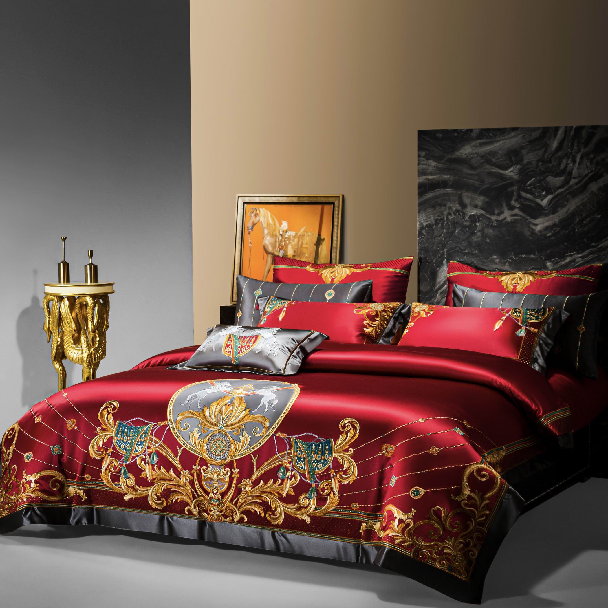 A striking bedding set in opulent red satin featuring elaborate golden embroidery and black accents, evoking a regal and sophisticated ambiance. The centerpiece showcases ornate shields, rearing horses, and intricate filigree patterns, complemented by matching embroidered pillowcases. To the side, a unique golden pedestal table with sculptural dragon-like details adds a touch of luxury, while a framed equestrian artwork and a black marble headboard enhance the room’s grand and stately design. The overall se