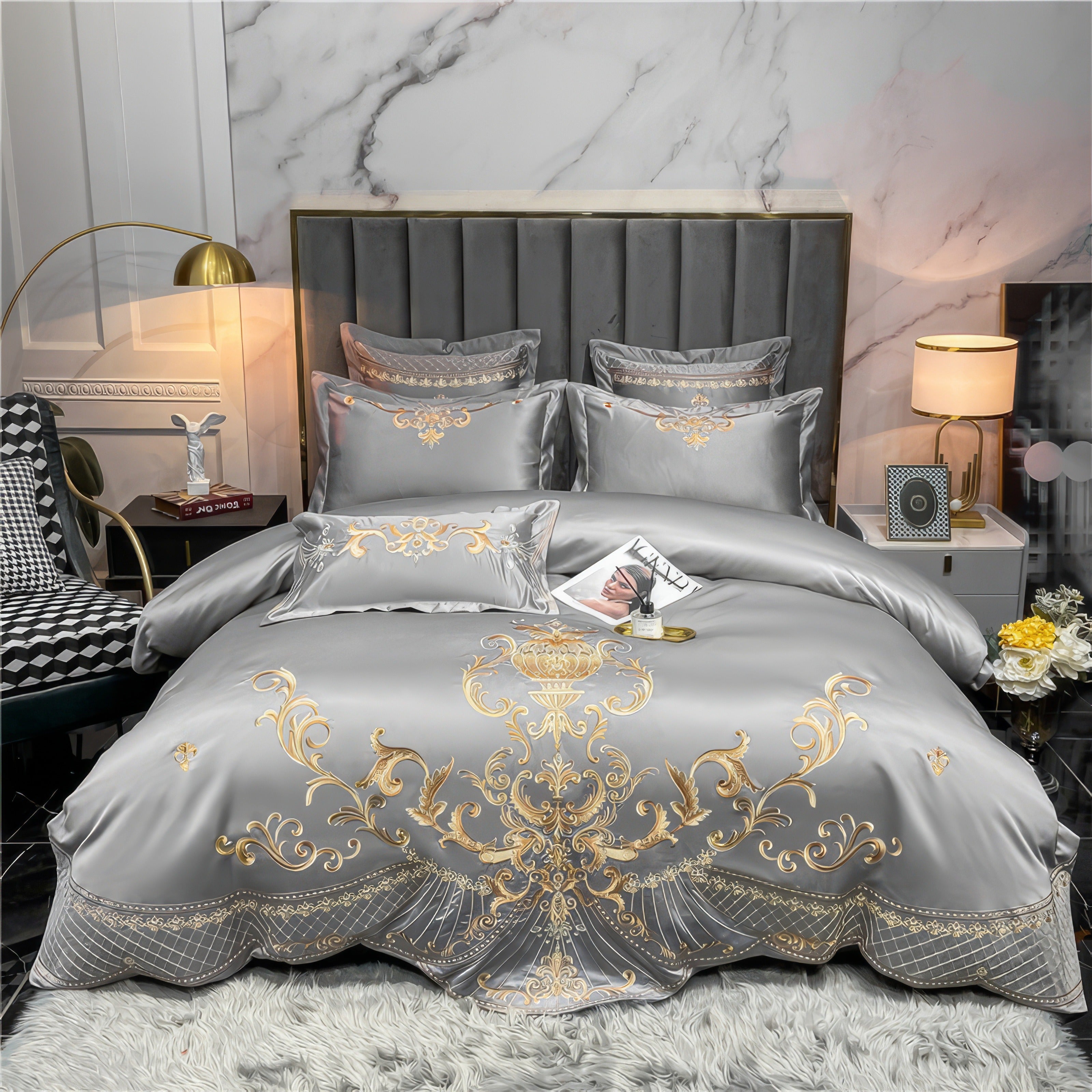 Luxurious silver bedding set made of Egyptian cotton with intricate gold embroidery, featuring ornate patterns across the duvet cover, pillowcases, and decorative cushions. The fabric has a soft sheen and smooth texture, elegantly draping over the edges of the bed.

