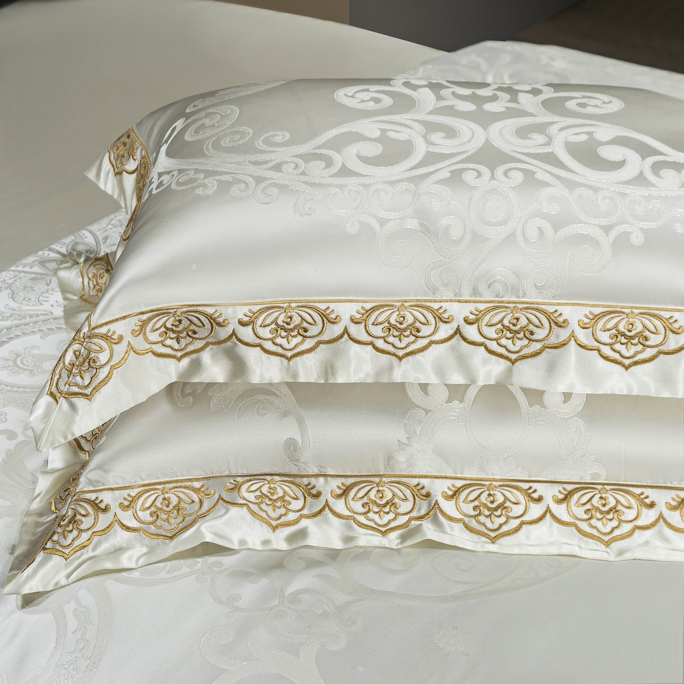 A close-up view of elegant white pillowcases featuring intricate gold embroidery along the edges. The swirling jacquard pattern complements the embroidered design, creating a luxurious and refined look. Perfect for adding a touch of sophistication to a high-end bedding ensemble.

