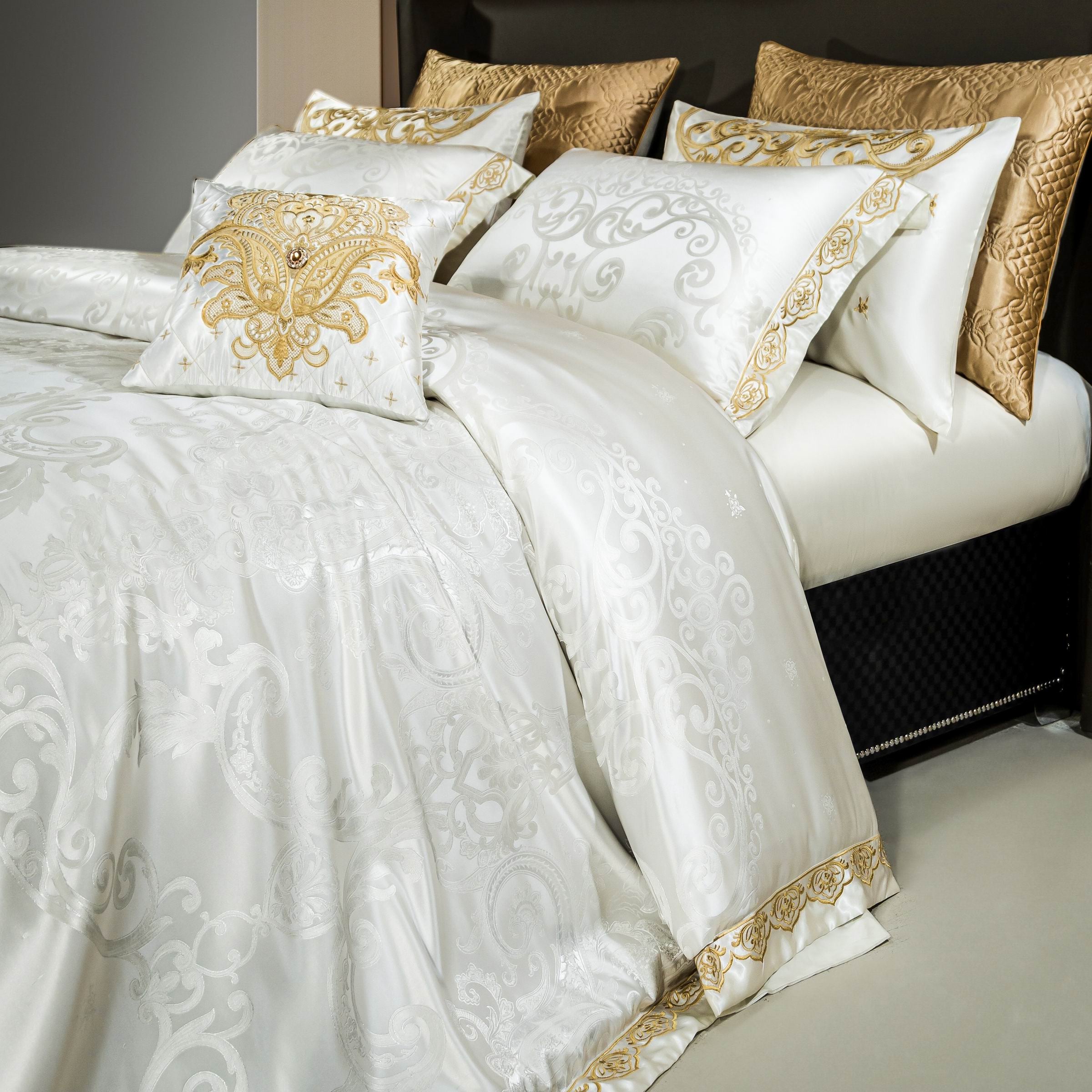 A close-up view of an opulent white bedding set with intricate gold embroidery and jacquard patterns. The set includes matching pillowcases with detailed golden accents and a central decorative cushion adorned with an ornate gold design and embellishments. The rich textures of the fabrics and the golden accent pillows enhance the luxurious aesthetic, exuding elegance and sophistication.

