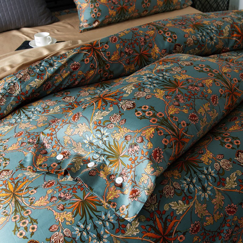 Teal bedding set featuring a vibrant botanical print with orange and red flowers, gold and green leaves, and intricate vine details. The fabric is draped with a pillowcase displaying white buttons and a coordinating duvet cover layered over a neutral tan sheet.

