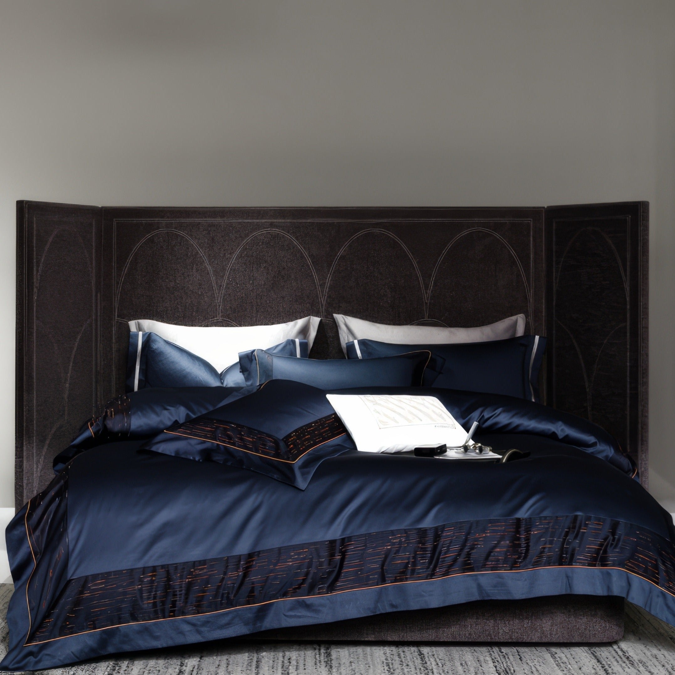 Modern luxury bedding set in deep navy blue, accented with textured black and red borders. The bed is adorned with layered pillow arrangements and a white decorative pillow at the center, placed against a dark, arched-panel headboard, creating a sophisticated and contemporary aesthetic.

