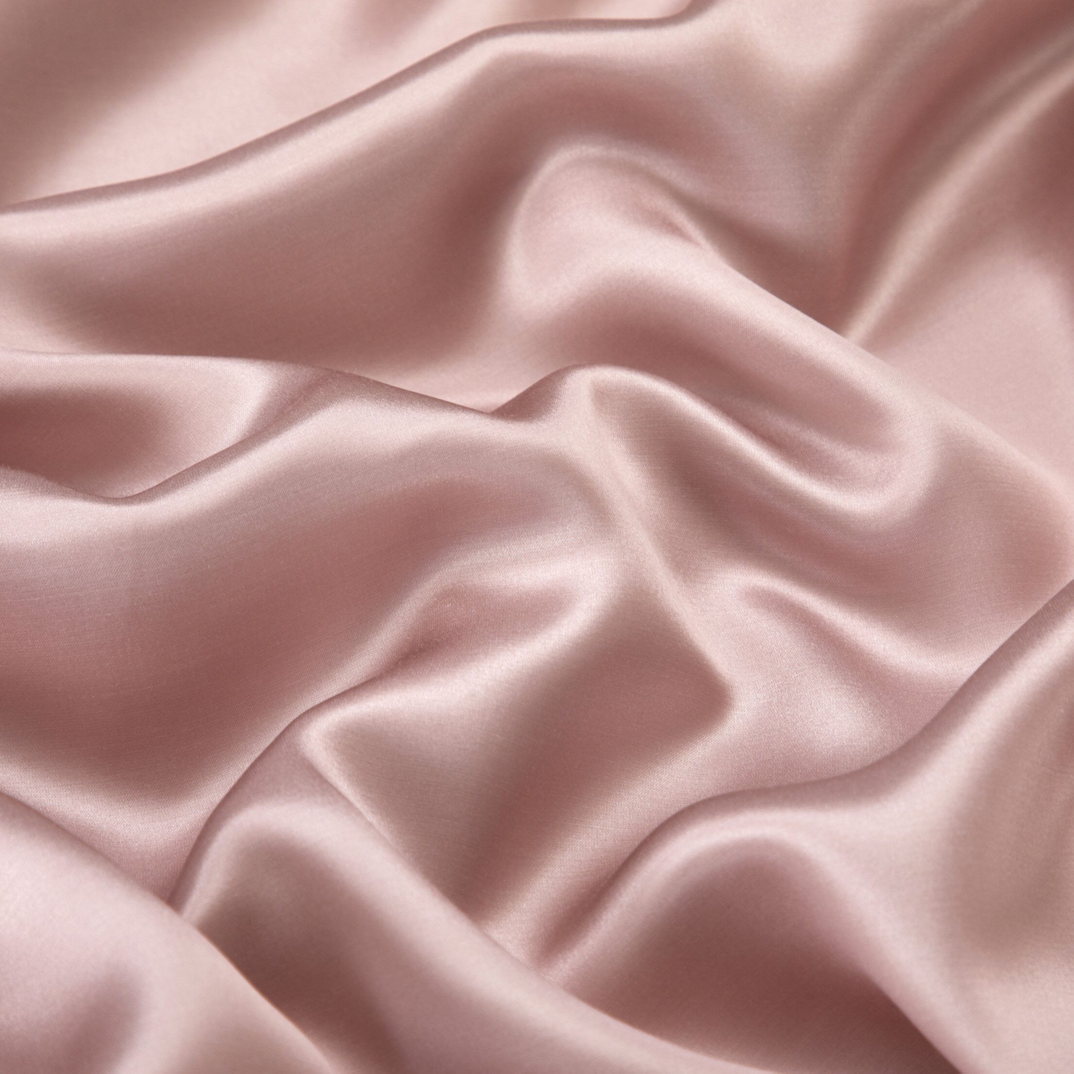 A detailed view of smooth blush pink silk fabric with a soft, flowing texture. The light elegantly reflects off the material's surface, emphasizing its glossy, luxurious finish and rich color tone.