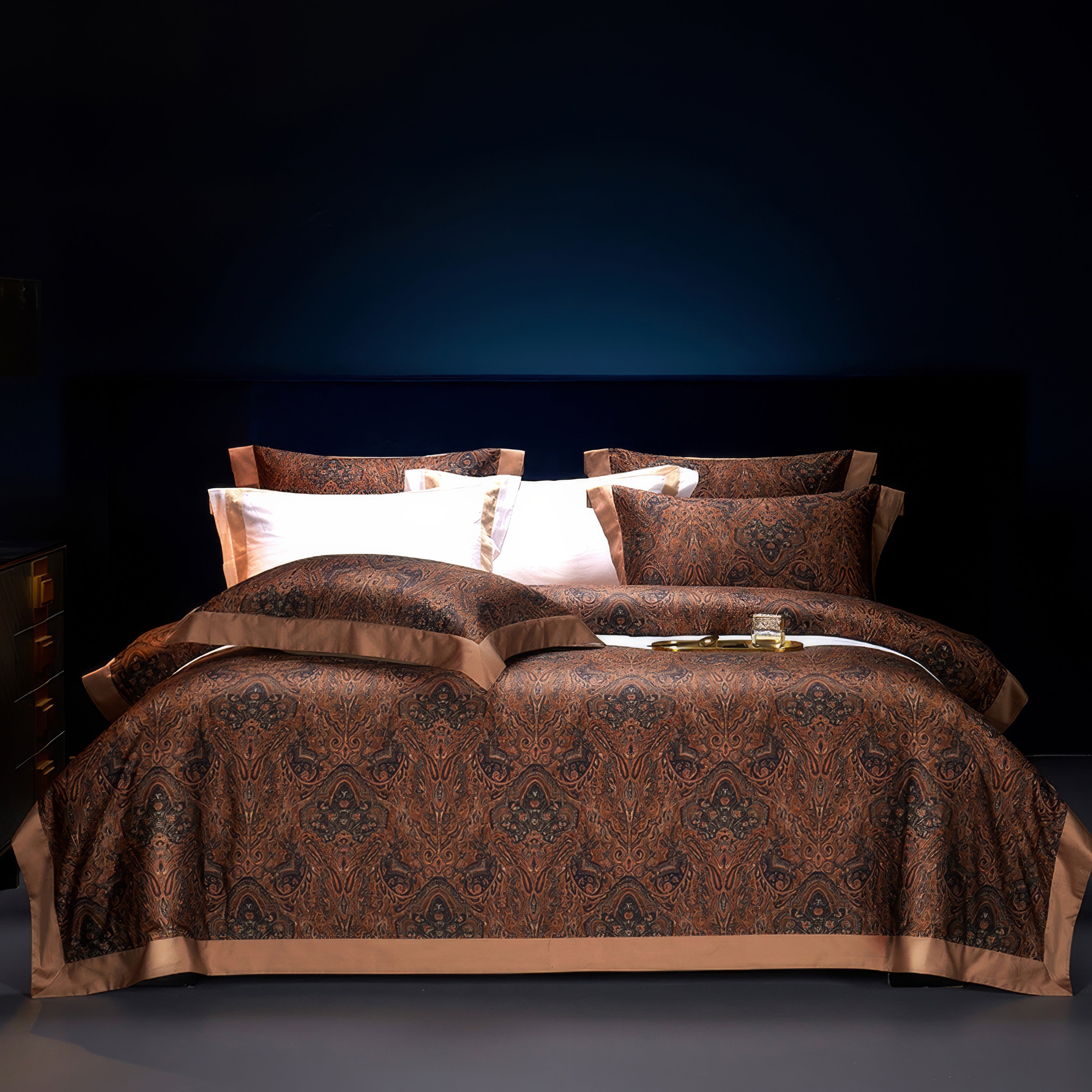 This bedding set showcases a luxurious and intricate paisley-inspired pattern in deep brown and black hues, accented by solid earthy brown borders. The set includes matching pillowcases and a duvet cover, which collectively create an opulent and sophisticated atmosphere. The dark, moody background enhances the richness of the fabric, exuding a warm, elegant aesthetic perfect for refined interiors. The texture appears plush and smooth, adding to the feeling of high-end comfort.

