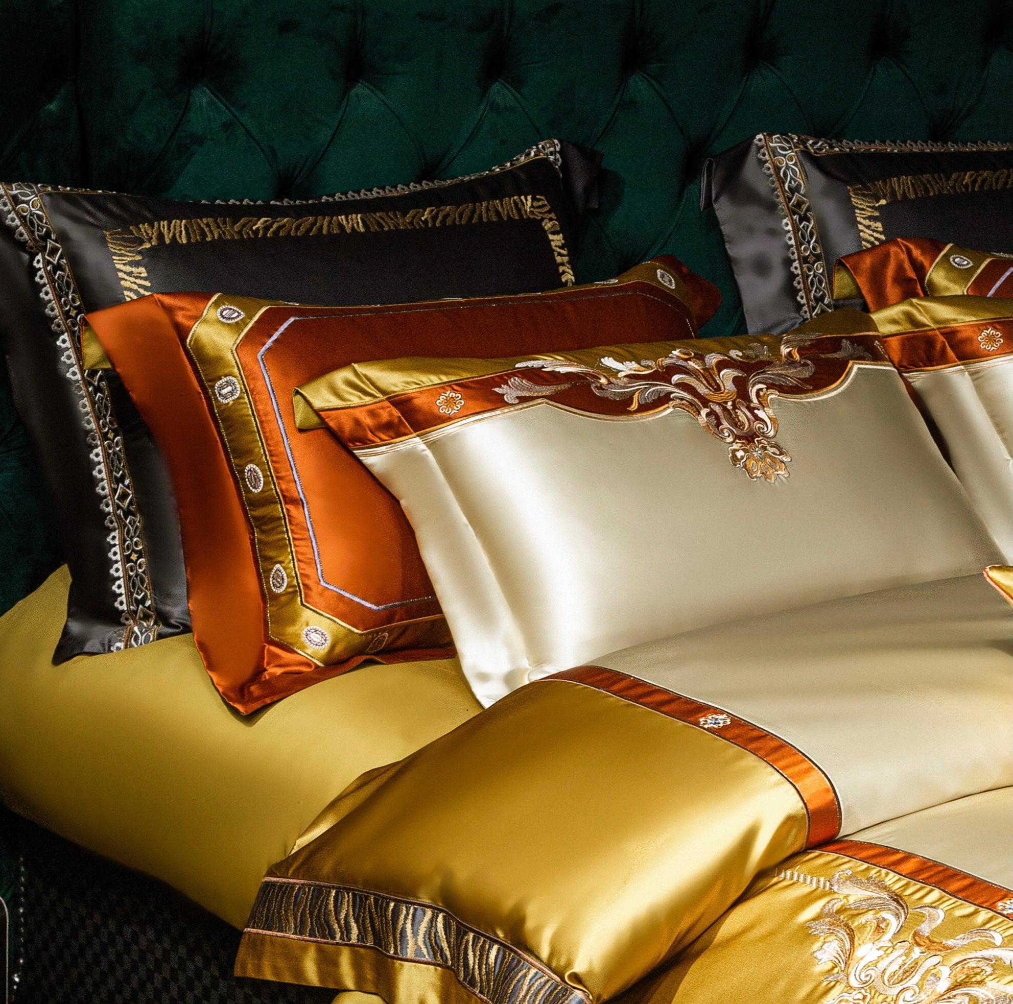 A close-up view of a luxurious bedding ensemble showcasing a rich blend of gold, ivory, and orange satin fabrics. The pillowcases feature elaborate baroque-style embroidery, accentuated by metallic trims and contrasting textures. Black pillowcases with intricate gold and animal print details provide depth and contrast, harmonizing with the vibrant orange and gold accents. The detailed craftsmanship emphasizes elegance and sophistication, making the bedding a standout centerpiece for a refined bedroom aesthe