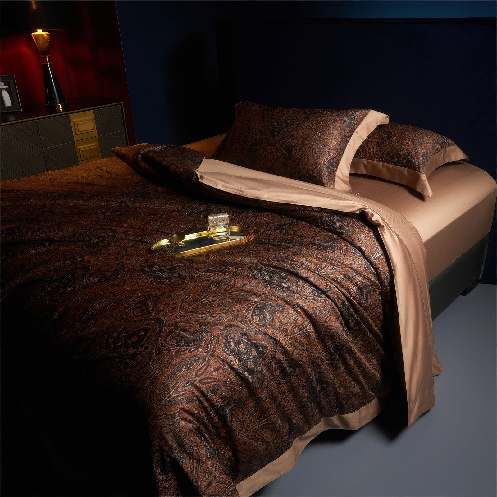 a luxurious bedding set featuring a sophisticated dark paisley pattern in deep brown and black tones, complemented by solid mocha-colored sheets and pillowcases. The fabric appears silky with a subtle sheen, enhancing the elegant aesthetic of the set. The bed is styled with a golden tray, adding a refined and glamorous touch to the overall ambiance. Perfect for high-end, moody interiors, this bedding evokes a sense of warmth, richness, and opulence, ideal for creating a cozy yet upscal