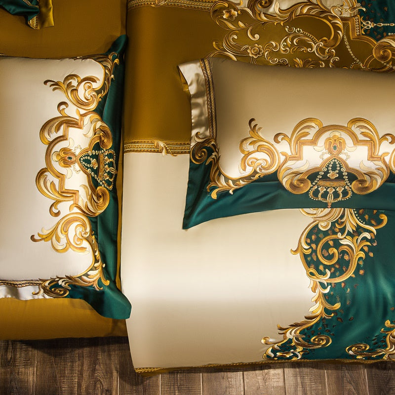 Flat lay view of pillowcases and a duvet cover featuring intricate golden embroidery with emerald green and cream tones. The ornate baroque patterns and elegant detailing exude luxury and sophistication.