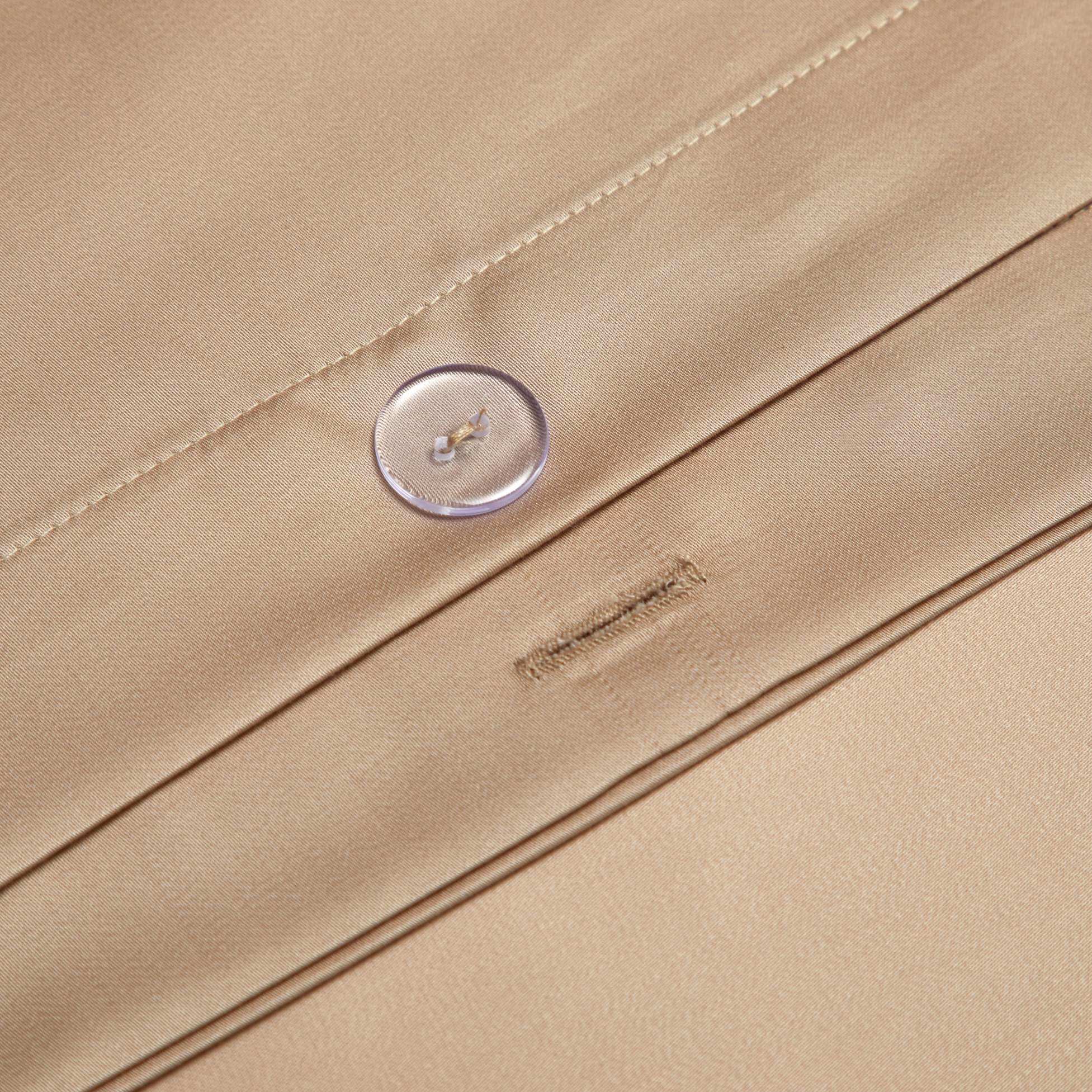 A close-up view of a champagne gold silk fabric detail, showcasing precise stitching and a clear button closure. The smooth, glossy finish of the material emphasizes its luxurious quality. The buttonhole is neatly tailored, ensuring durability and elegance in design.