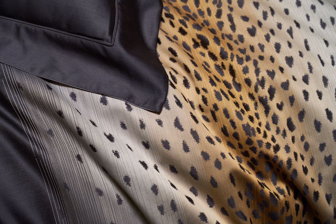 Close-up of a leopard print gradient pattern transitioning from gold to charcoal tones on smooth, luxurious fabric.

