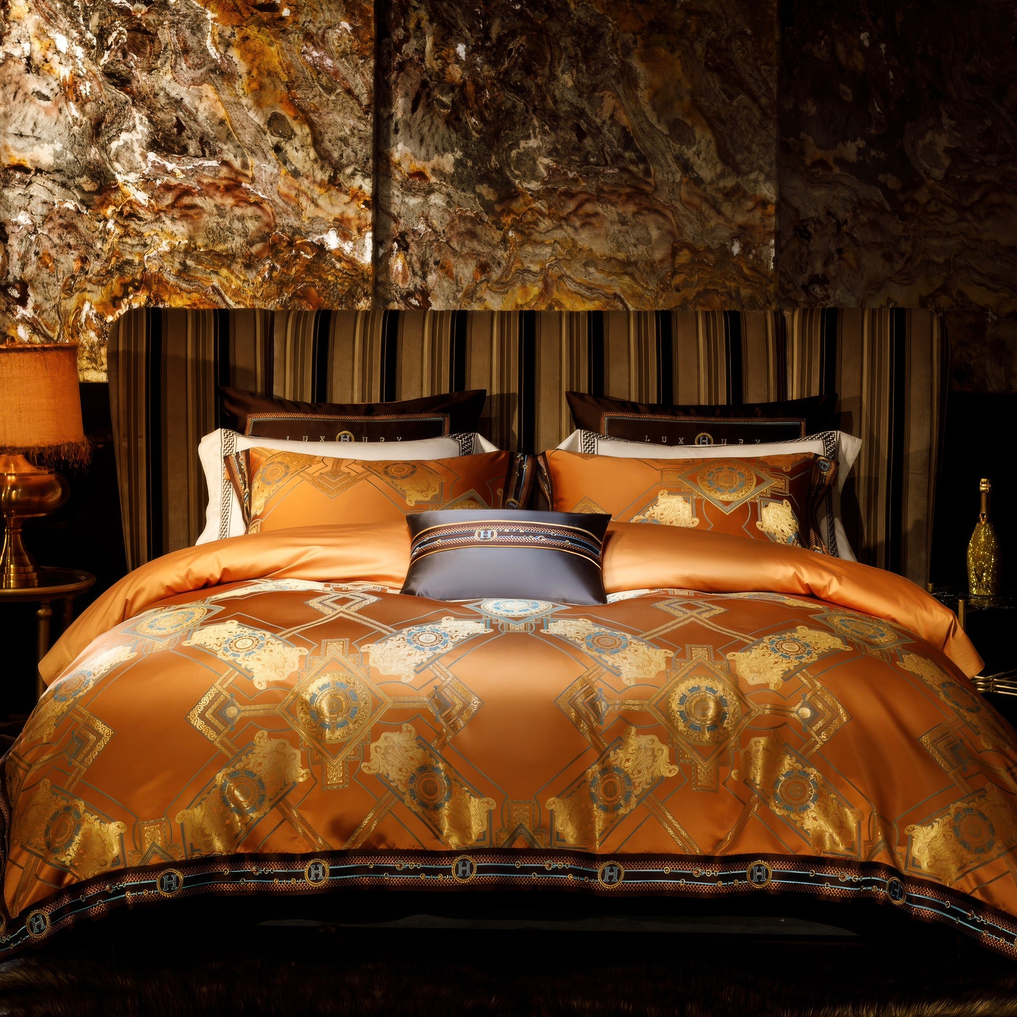 A luxurious bedding setup featuring a vibrant orange duvet adorned with intricate golden geometric patterns and accents of blue. The bed is styled with matching pillows and a complementary striped headboard. A marble-textured wall provides an opulent backdrop, with a warm-toned lamp and a gold decorative bottle on the bedside table enhancing the elegant and sophisticated ambiance.