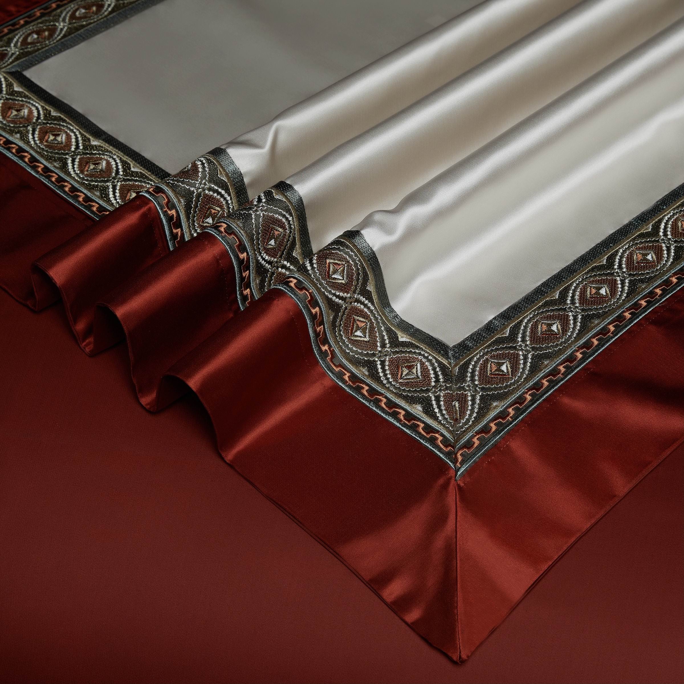 A detailed close-up of a luxurious bedspread showcasing a rich ivory center bordered with vibrant crimson red and intricate olive green embroidery. The finely crafted design includes geometric and ornate patterns that add depth and elegance, seamlessly blending bold and subtle elements. The bedspread is carefully folded to display its soft, smooth texture and precise craftsmanship, set against a deep crimson backdrop for a dramatic and opulent effect.