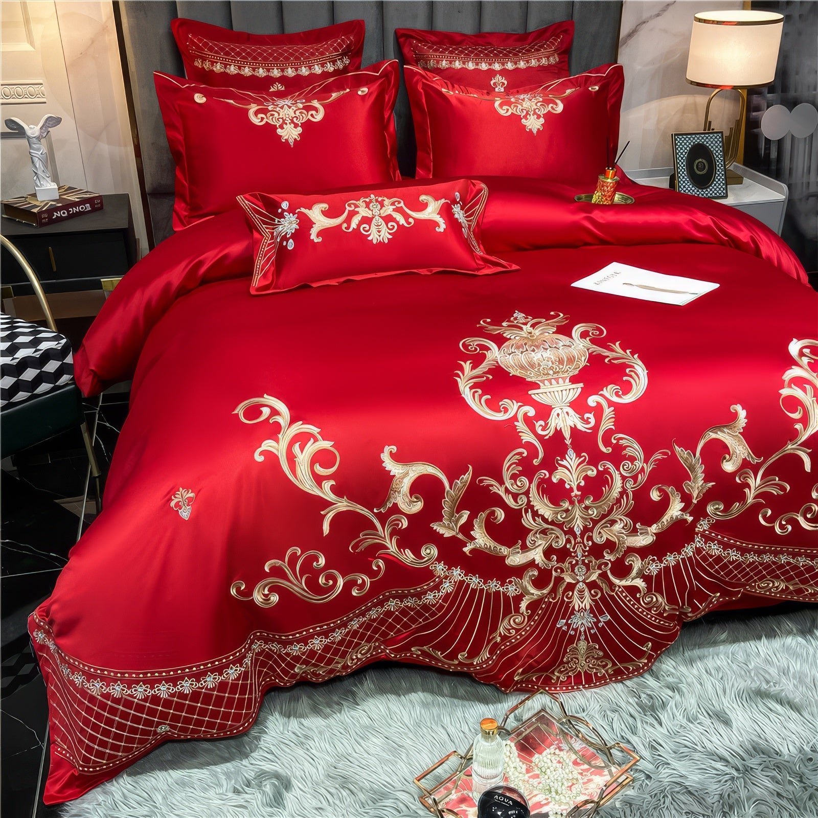 Red Egyptian cotton bedding set with gold embroidery featuring intricate floral and scrollwork patterns. The rich red fabric highlights the luxurious sheen of the Egyptian cotton material, complemented by matching pillowcases and an embroidered duvet cover. The bedding is styled against a grey upholstered headboard, with a modern bedside setup and soft grey rug adding a cozy, elegant feel to the room.

