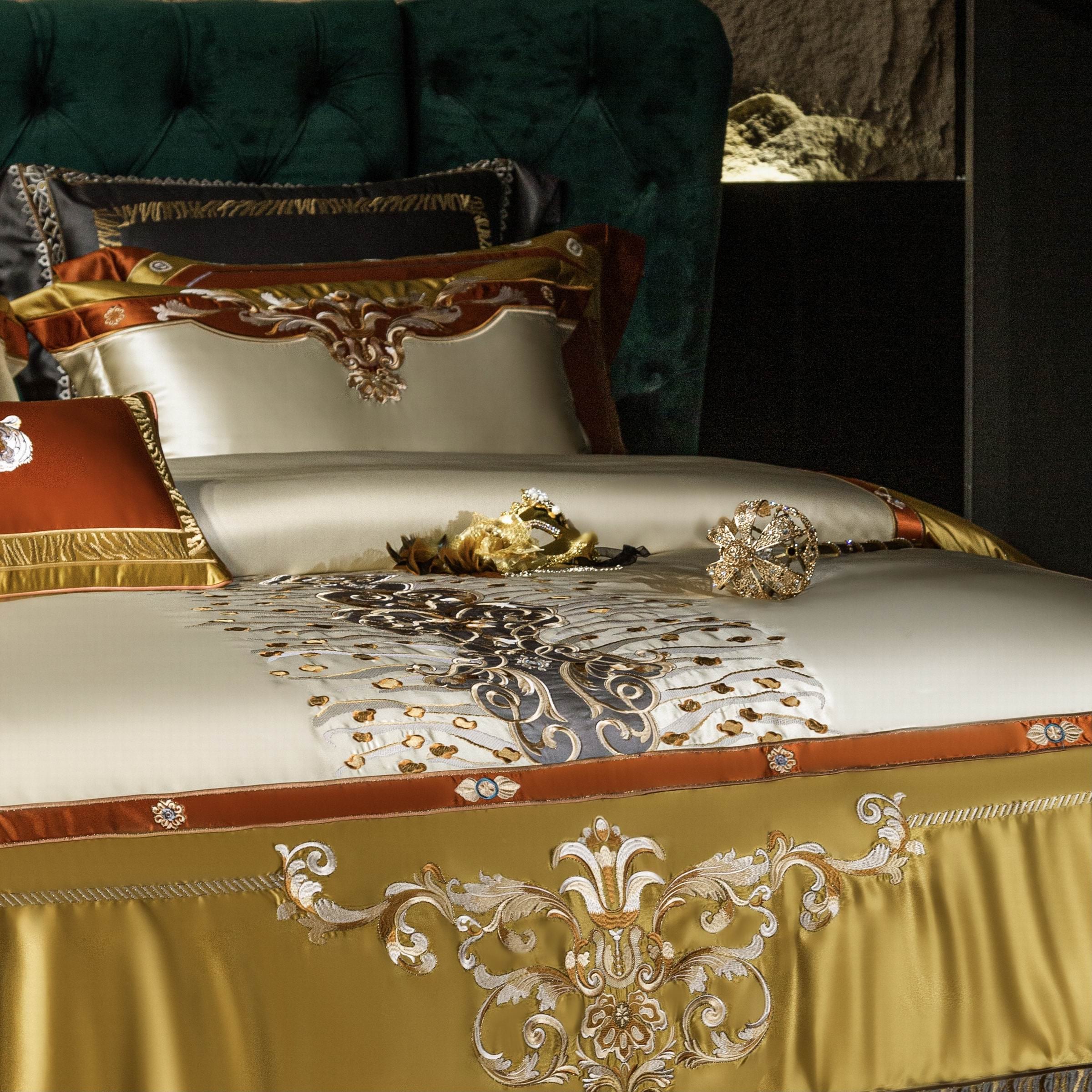 A luxurious bedding set featuring rich golden and ivory tones with ornate embroidery and intricate embellishments. The duvet cover showcases a regal central design with baroque-style motifs in gold and dark accents, complemented by matching pillowcases adorned with bold, elegant details. A decorative golden and black mask adds a touch of drama and sophistication to the scene. The plush, tufted emerald green headboard provides a lavish backdrop, enhancing the opulence of the setting.