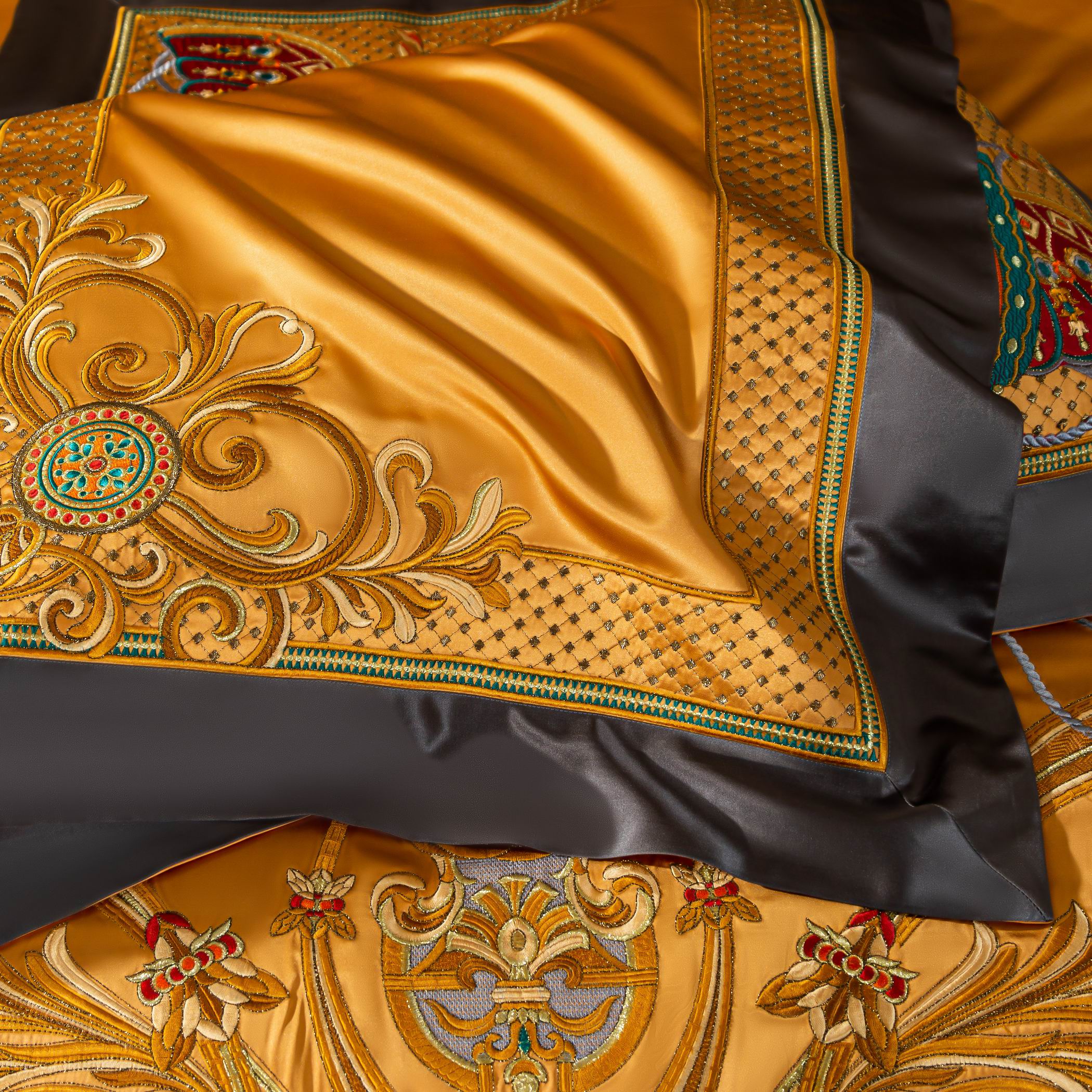 A detailed close-up of a golden-yellow luxury bedding set showcasing its intricate baroque-inspired embroidery. The design features elaborate golden scrolls and floral motifs intertwined with circular accents in vibrant red and green hues. A dotted pattern decorates the borders, complemented by sleek black trim that adds a sophisticated contrast. The smooth satin texture enhances the richness of the design, while the embroidery demonstrates exceptional craftsmanship, exuding an opulent and regal charm.