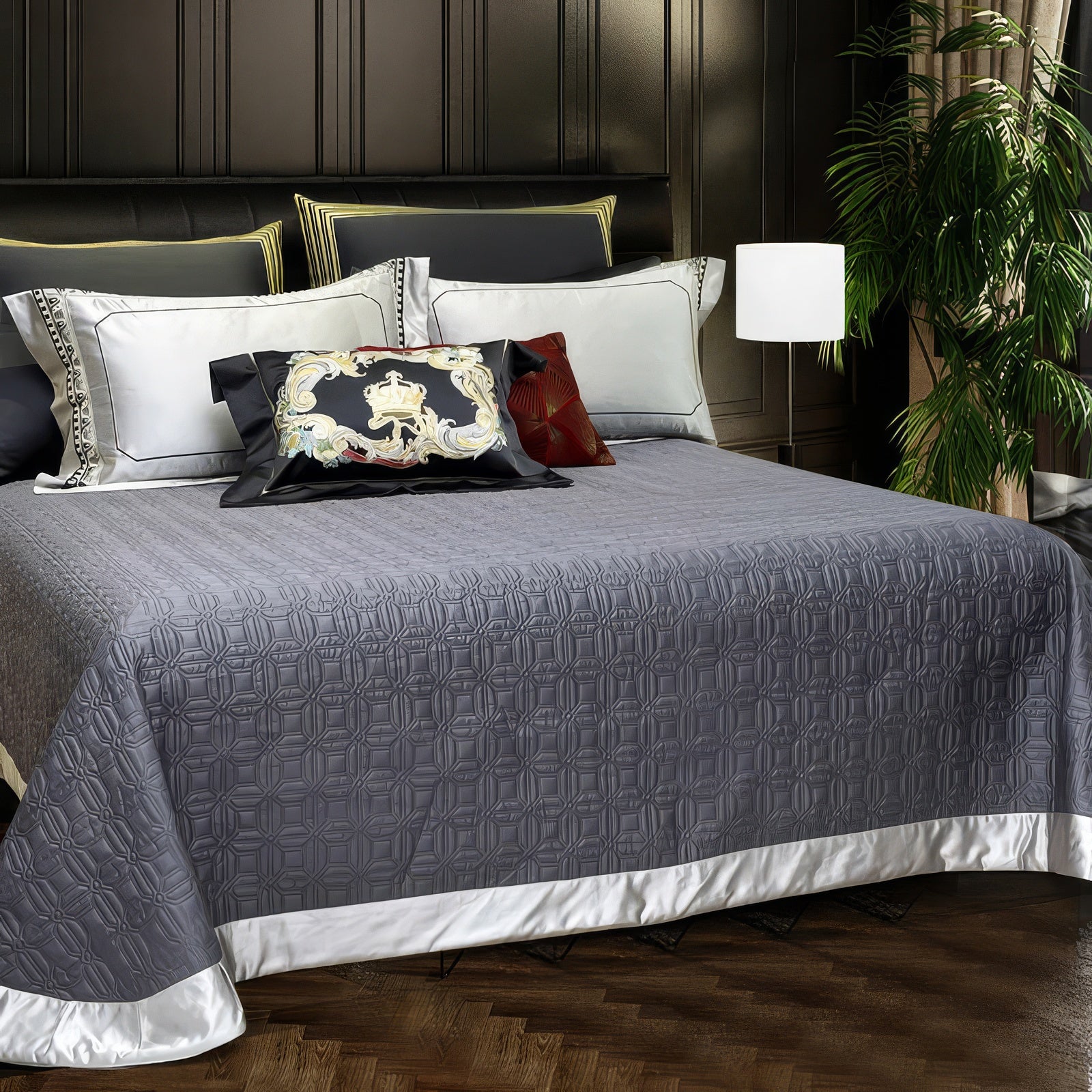 A textured slate-gray quilt with a geometric pattern, bordered by a crisp white trim, adds a touch of understated elegance. Complemented by accent pillows in black, gold, and red designs, the bedding creates a balanced blend of luxury and modern sophistication, set against a dark-paneled wall and surrounded by lush greenery.

