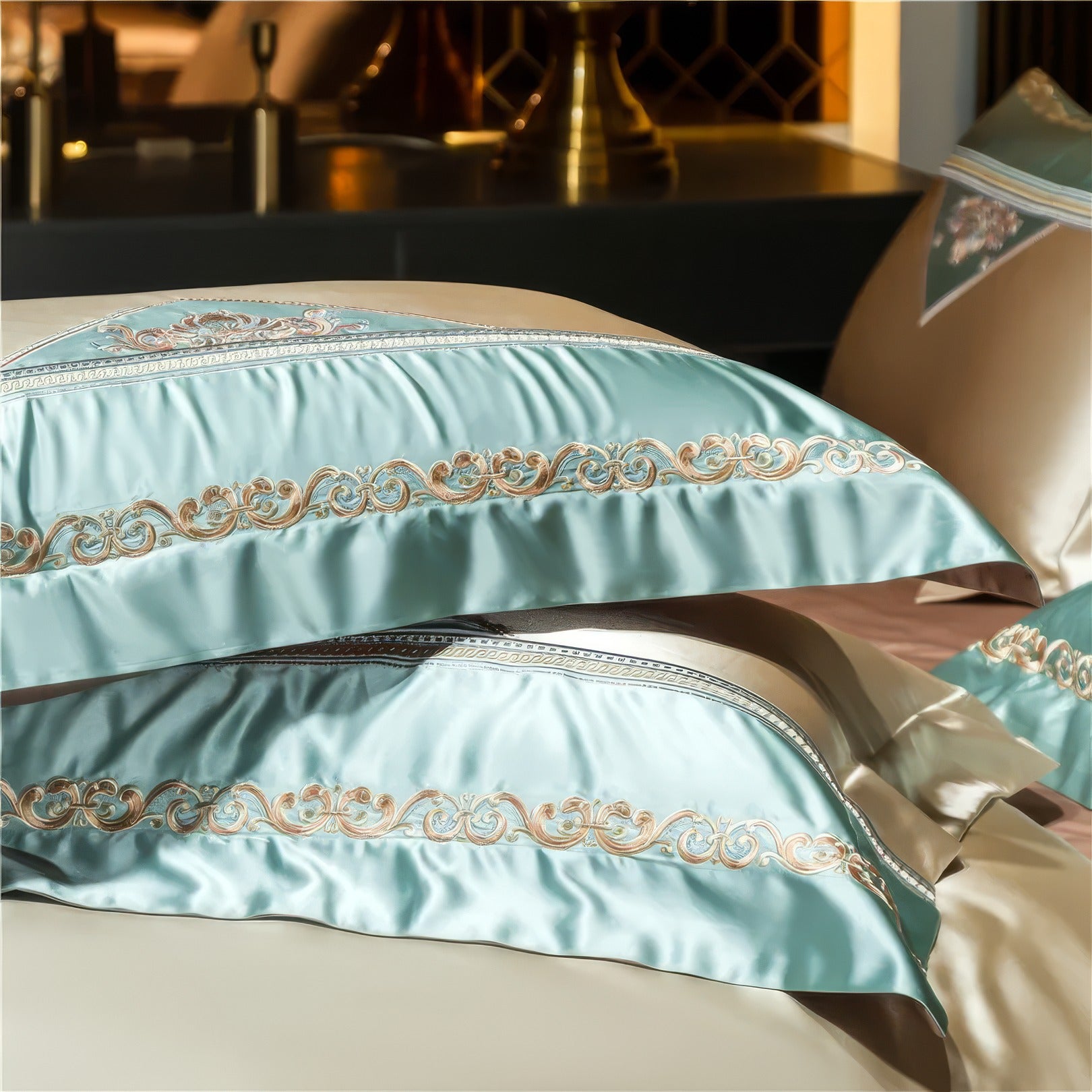 Close-up view of luxurious satin pillowcases in a soft blue shade, adorned with intricate gold embroidery patterns, elegantly displayed with beige accents in a sophisticated bedroom setting.

