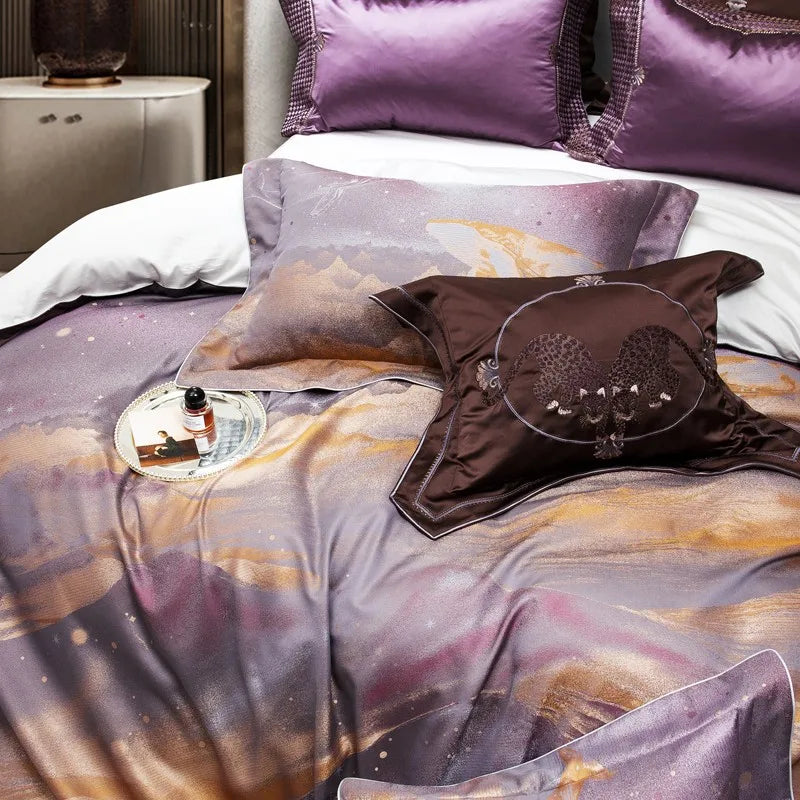 The bed features a luxurious set of bedding with a blend of purple and golden tones, adorned with an abstract and celestial design. The centerpiece includes a dark brown decorative pillow embroidered with a detailed double-leopard motif, bordered elegantly with piping. Complementary purple pillows and a duvet add richness to the ensemble. A silver tray with pearl detailing holds a perfume bottle and photograph, creating a refined and opulent ambiance.