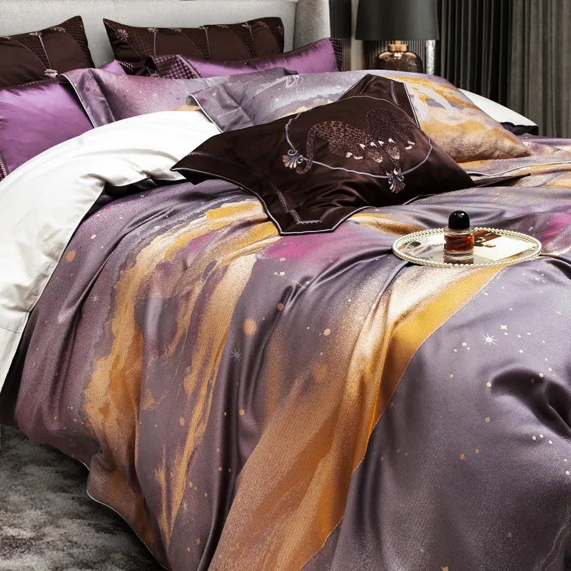 The bedding showcases a dreamy blend of purple and golden hues with a celestial-inspired design. The rich fabric reflects a subtle shimmer, adding depth to the color palette. A dark brown pillow with an embroidered double-leopard motif serves as a striking focal point. A white duvet peeks from underneath, enhancing the contrast. A silver tray with pearl accents, holding a perfume bottle, adds a touch of elegance and sophistication.