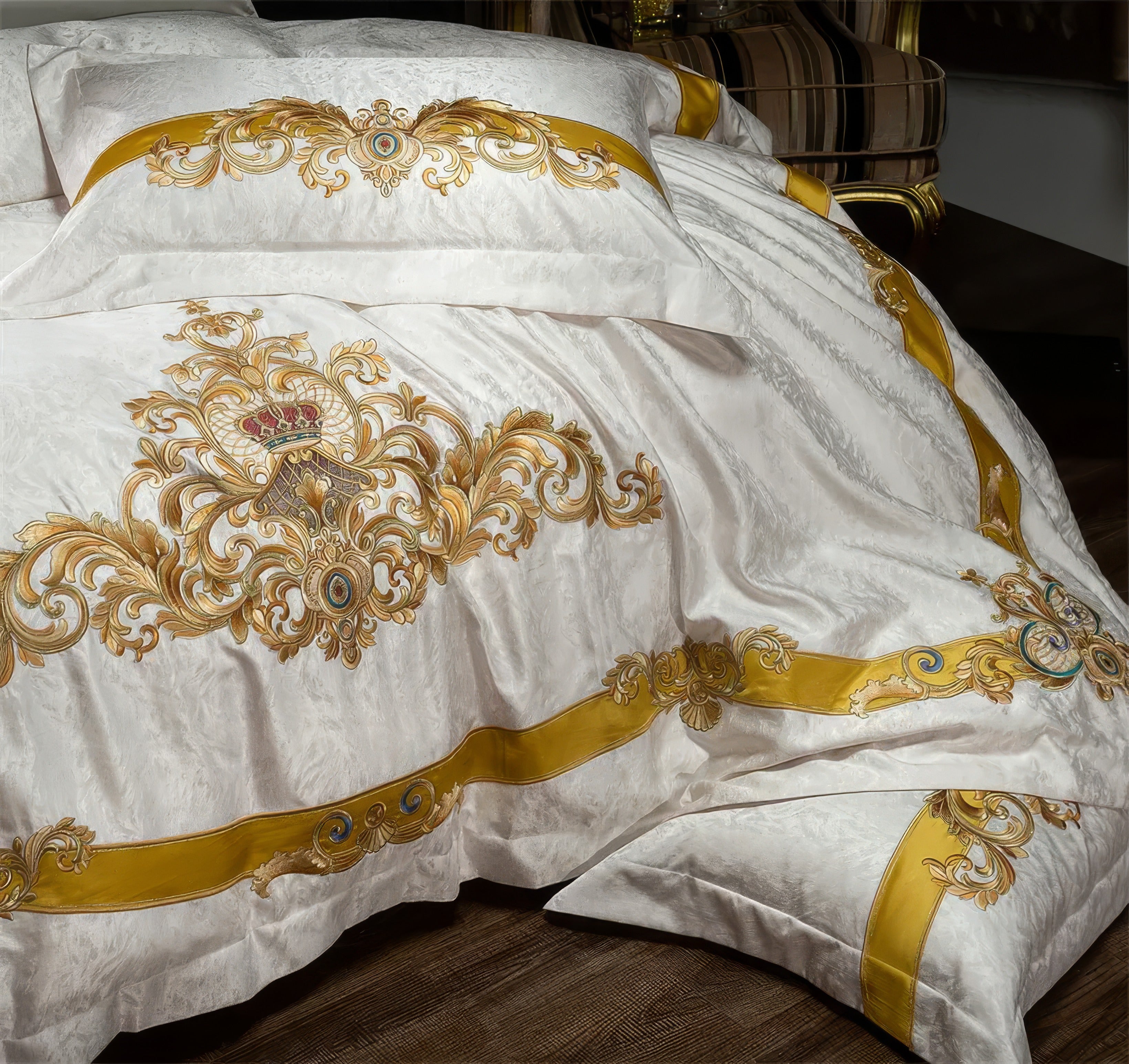 A detailed view of a luxurious bedding set highlighting exquisite golden embroidery on a silky white base. The design features ornate baroque-style patterns with regal crowns and intricate swirls, enhanced by a striking golden ribbon accent. The rich textures and elegant craftsmanship exude sophistication, perfect for elevating a royal-themed bedroom decor.