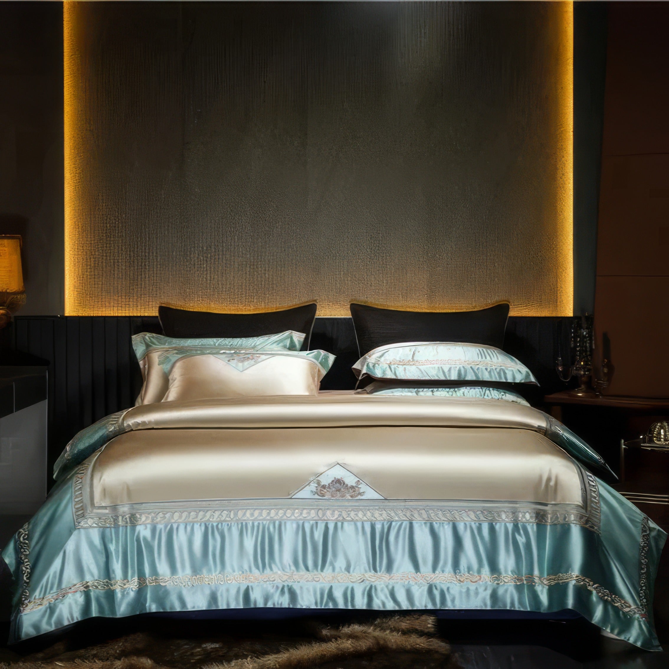 Luxurious bedding set featuring a satin blue duvet cover with beige accents and intricate embroidery, elegantly displayed in a dimly lit modern bedroom with a golden ambient wall light and contrasting black pillows.

