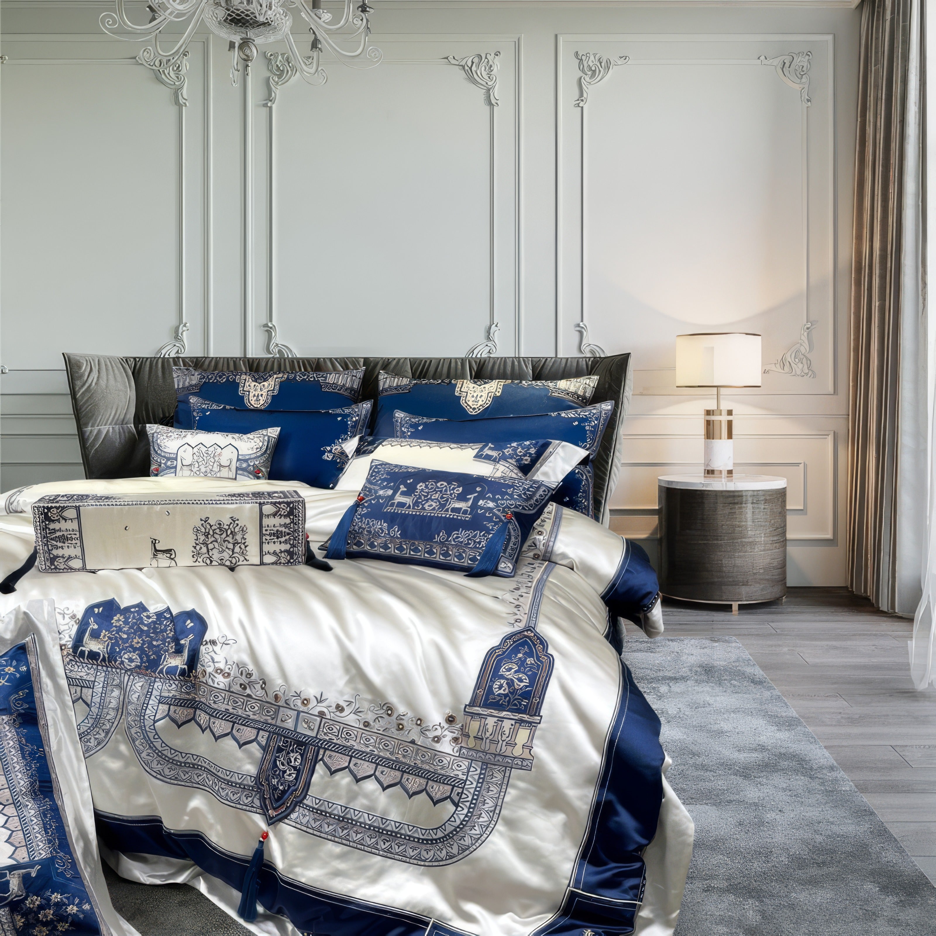 Luxurious bedroom featuring ornate white paneled walls, a plush silver-gray bed frame, and opulent blue and white embroidered bedding with intricate tassel and floral details, complemented by a modern side table and elegant lighting.