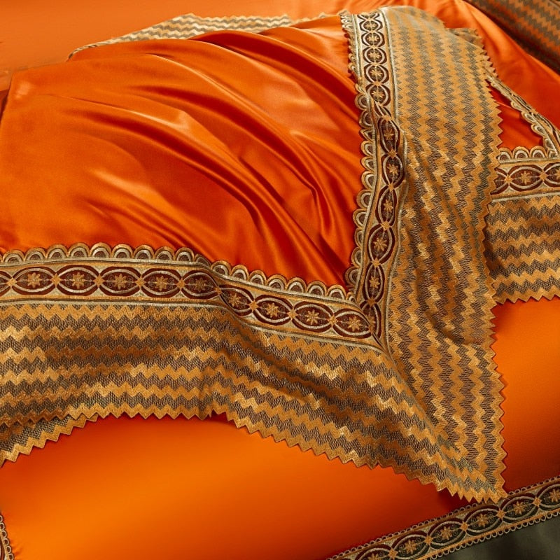 Bright orange satin bedding with an intricate decorative border featuring a chevron pattern in shades of gold, brown, and black. The fabric appears smooth and glossy, draped with folds, emphasizing its luxurious texture.

