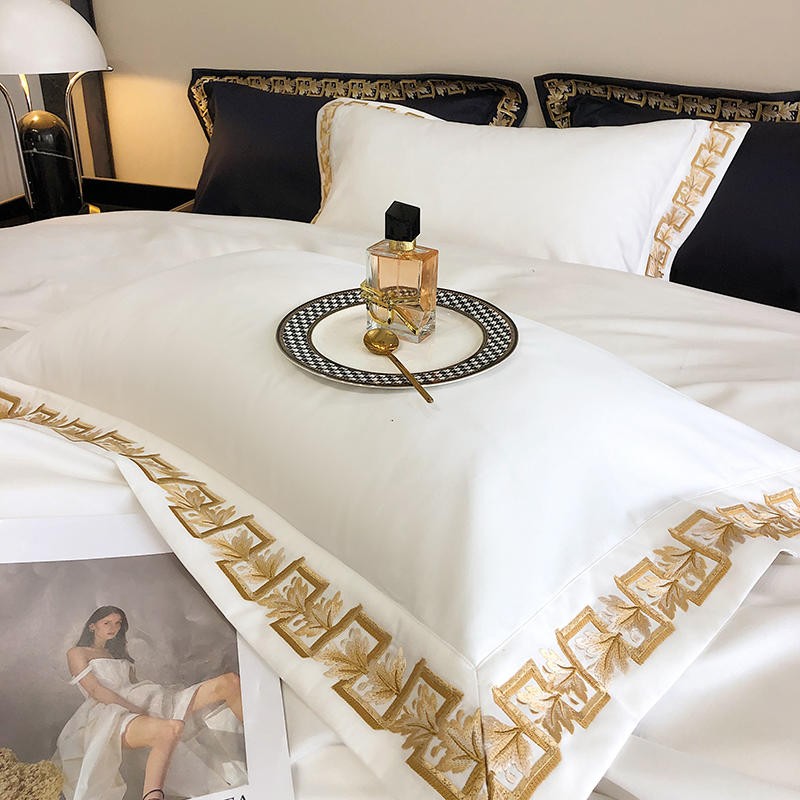 Egyptian cotton pillowcase in white featuring intricate gold embroidery, styled with a luxury perfume bottle, a patterned plate, and a gold spoon for a sophisticated presentation.

