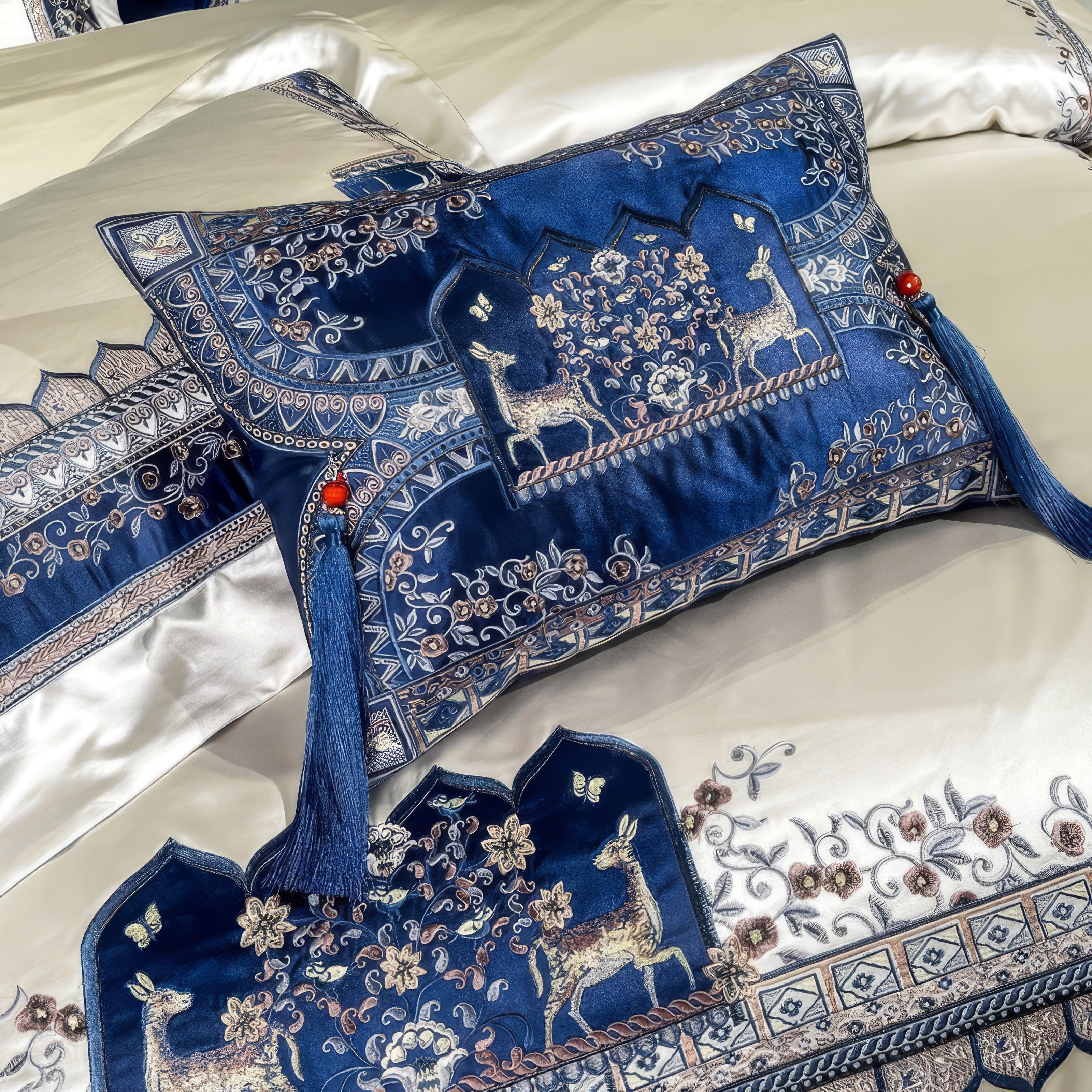 A luxurious silk pillow adorned with intricate embroidery of golden deer and delicate floral patterns on a rich royal blue background, enhanced with red tassels for a regal touch, complementing an elegant bedding ensemble.