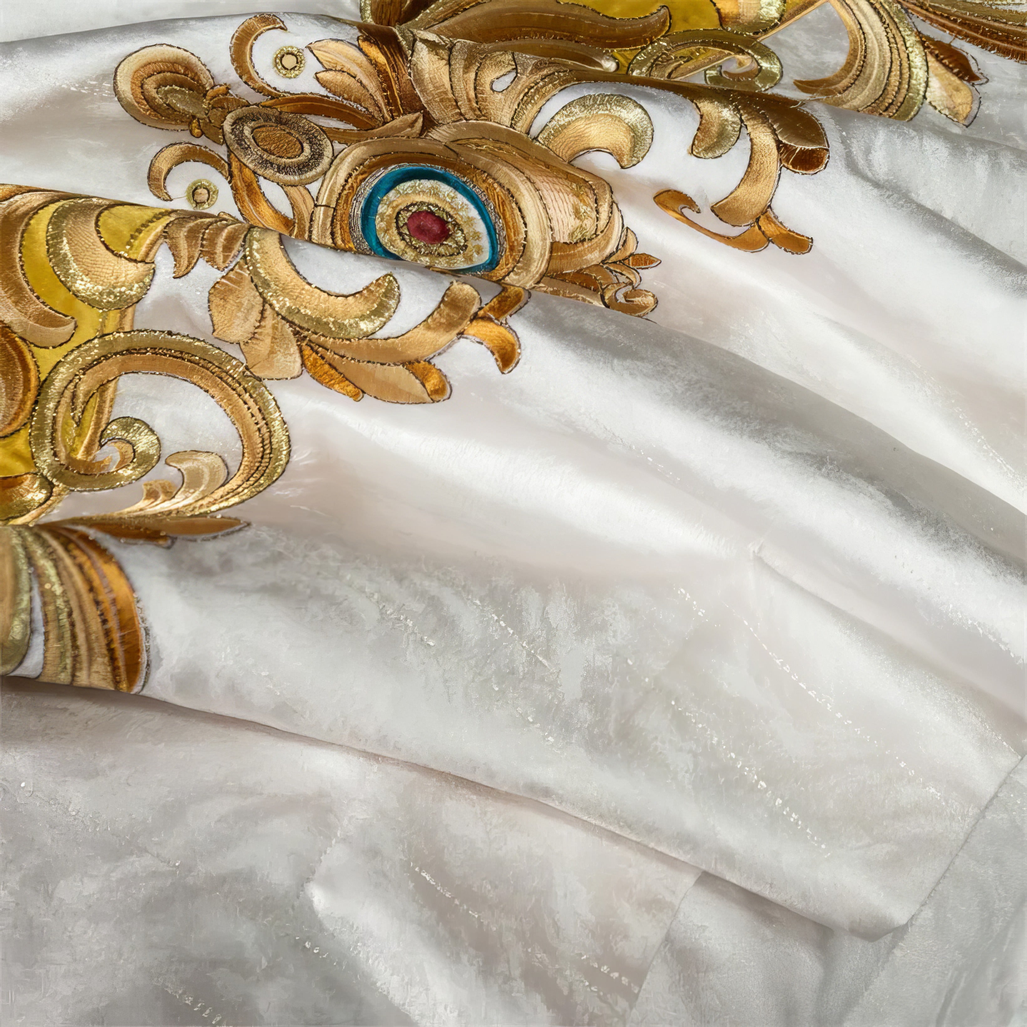 A close-up of intricate golden embroidery featuring baroque-inspired swirls, accented with vibrant blue and red gemstone-like embellishments on a luxurious white fabric. The fine details and shimmering texture emphasize the craftsmanship, adding an opulent touch to the overall design.