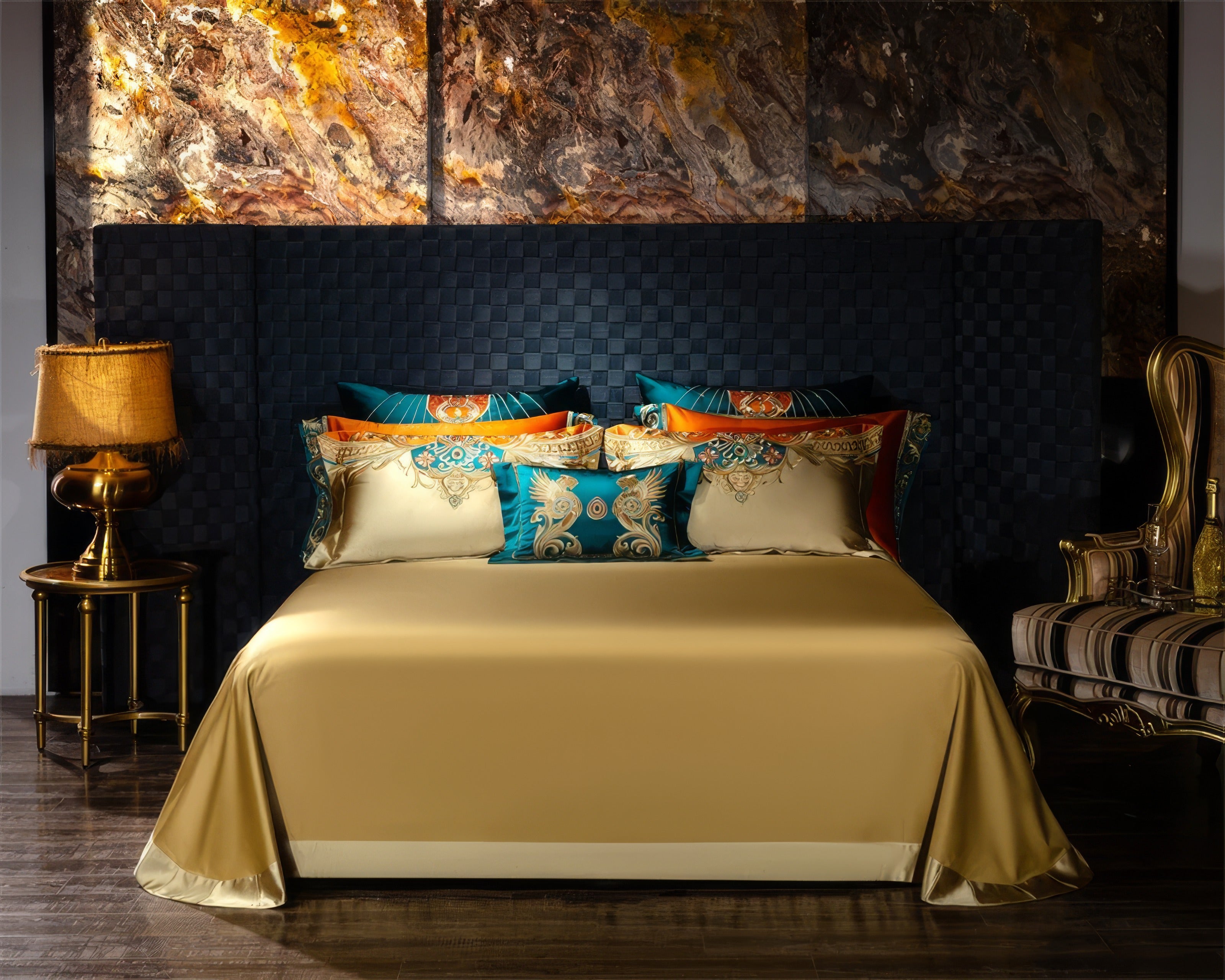 A regal bedroom setup featuring a golden satin bedding set adorned with a minimalist yet elegant design. The backdrop showcases a woven navy-blue headboard that adds depth and texture to the scene, complemented by a richly veined marble-patterned wall with warm gold and brown hues. The vibrant teal and orange accent pillows display intricate baroque-inspired embroidery, creating a luxurious contrast against the plain golden bedspread. A golden lamp with a fringed shade sits atop a round side table, casting 