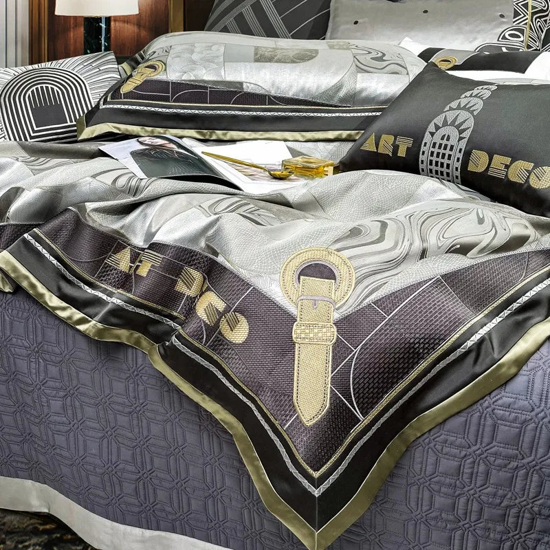 Elegant Art Deco bedding set showcasing a sophisticated mix of silver, grey, and black tones with intricate patchwork patterns. The design features gold accents, including a key motif and the 'Art Deco' inscription on the border, adding a luxurious touch. The quilted base layer complements the ensemble, creating a cohesive and refined look in a modern bedroom setting.