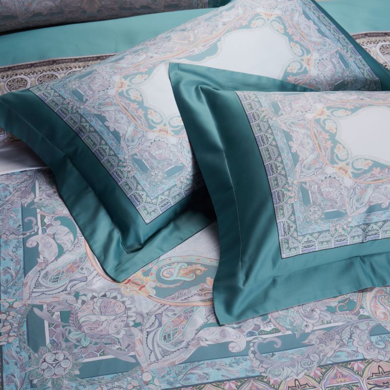 Two pillowcases in turquoise with ornate pastel patterns, displaying a seamless blend of elegance and luxurious fabric design.

