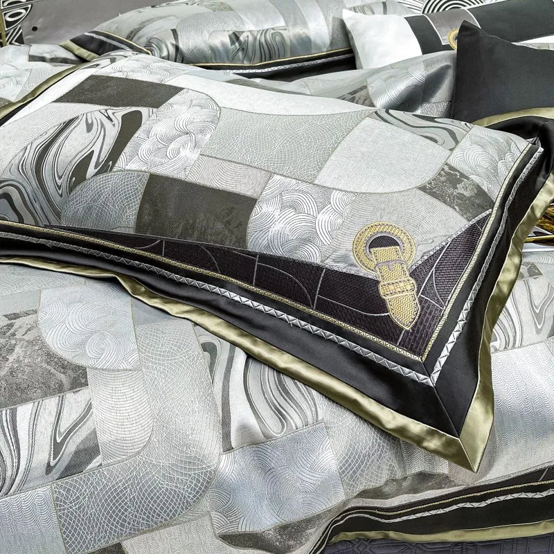 Close-up view of a pillow from the Art Deco bedding set, highlighting the intricate geometric patchwork design in silver, black, and grey tones. The pillow features a unique buckle-like embroidery in gold thread, adding a touch of elegance and sophistication to the overall design. The silky sheen of the fabric enhances the luxurious aesthetic.