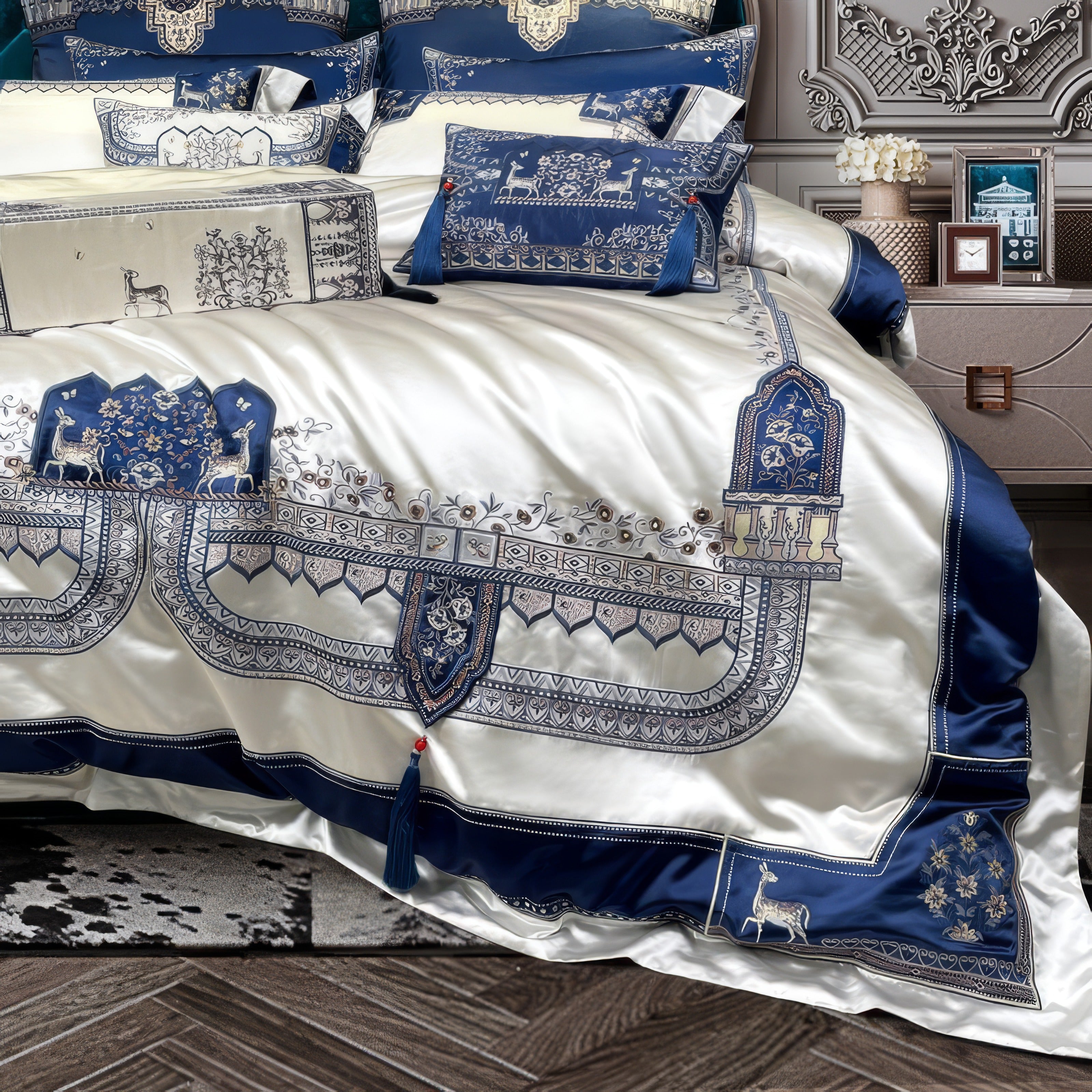 Luxurious bedding set showcasing intricate blue and white embroidery with tassel accents and elegant deer motifs, laid on a silky white fabric, complemented by a plush gray carpet and rich wooden flooring for a sophisticated bedroom look.