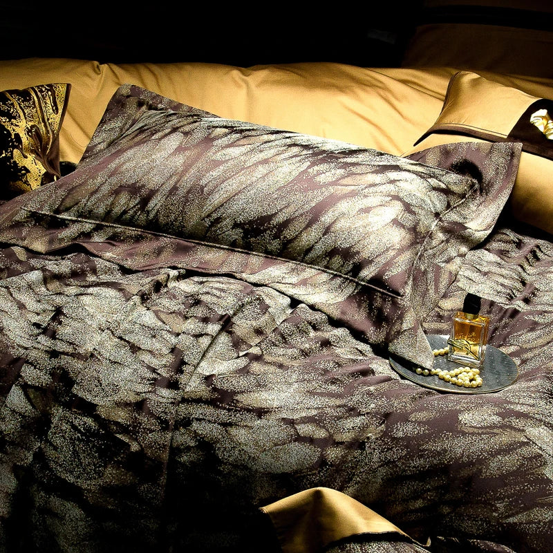 An intricately designed bedding set showcasing a sophisticated dark brown and silver feather-inspired pattern. The bedding is complemented by golden accents in the background and a golden perfume bottle placed on a silver tray adorned with a pearl necklace. This luxurious composition exudes opulence and modern elegance, perfect for a high-end bedroom setup or a premium bedding advertisement.