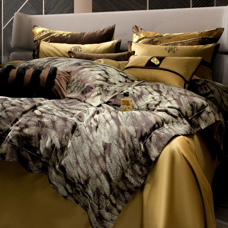 A luxurious bedding set with an intricate feather-pattern design in deep brown and golden tones, exuding elegance and richness. The duvet cover's textured look is complemented by matching pillows featuring embroidered and gold-accented details. The bedding arrangement includes a soft golden bedsheet, creating a warm and opulent color palette. A small perfume bottle on the bed adds a touch of glamour, while the sleek, modern headboard in the background enhances the sophisticated bedroom ambiance.