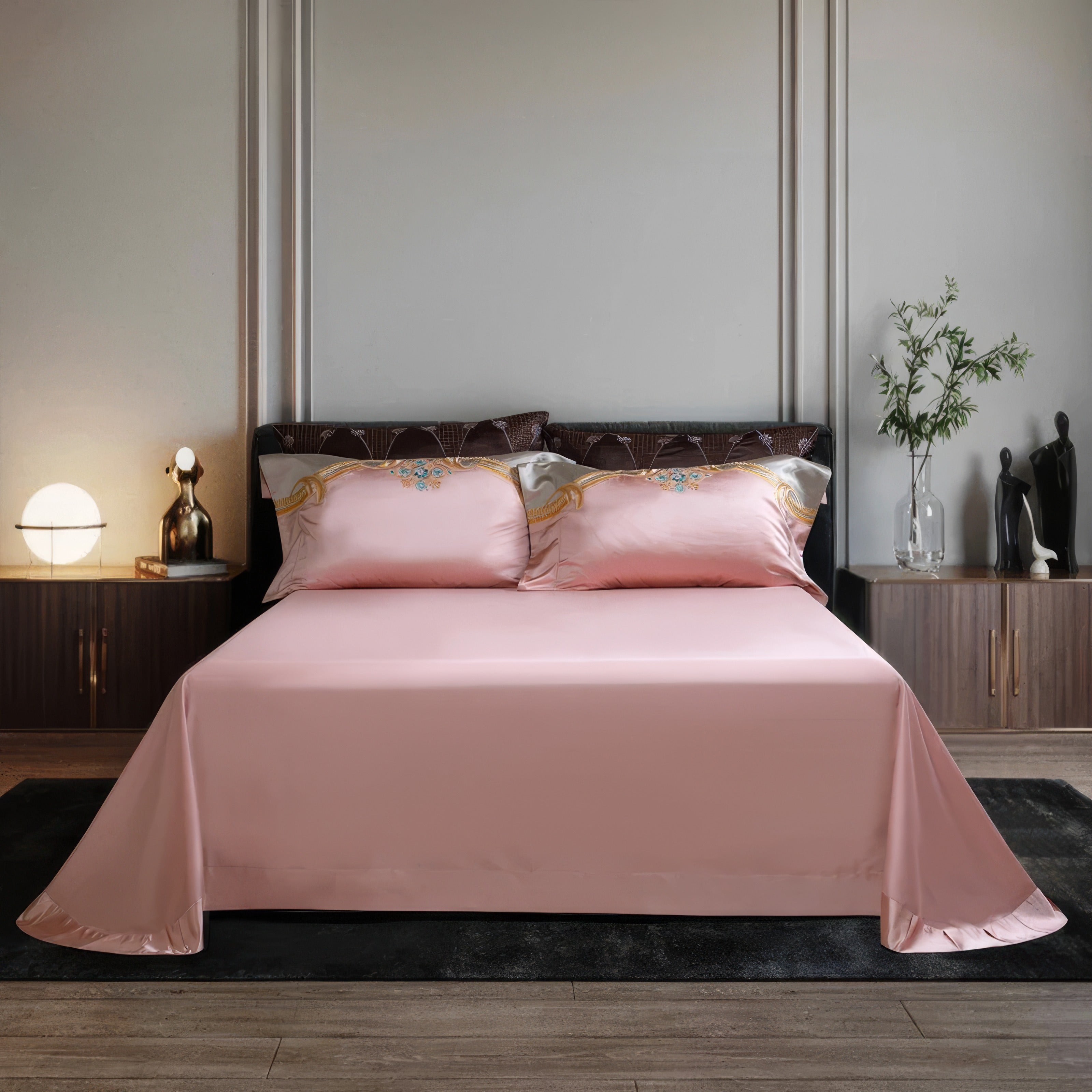 A neatly arranged luxury bedding set featuring soft pink sheets with a smooth and lustrous finish. The pillowcases display elegant embroidery with intricate golden patterns and accents of blue jewels. The backdrop includes a minimalistic bedroom setting with modern decor, soft lighting, and neutral tones, enhancing the serene and sophisticated ambiance.