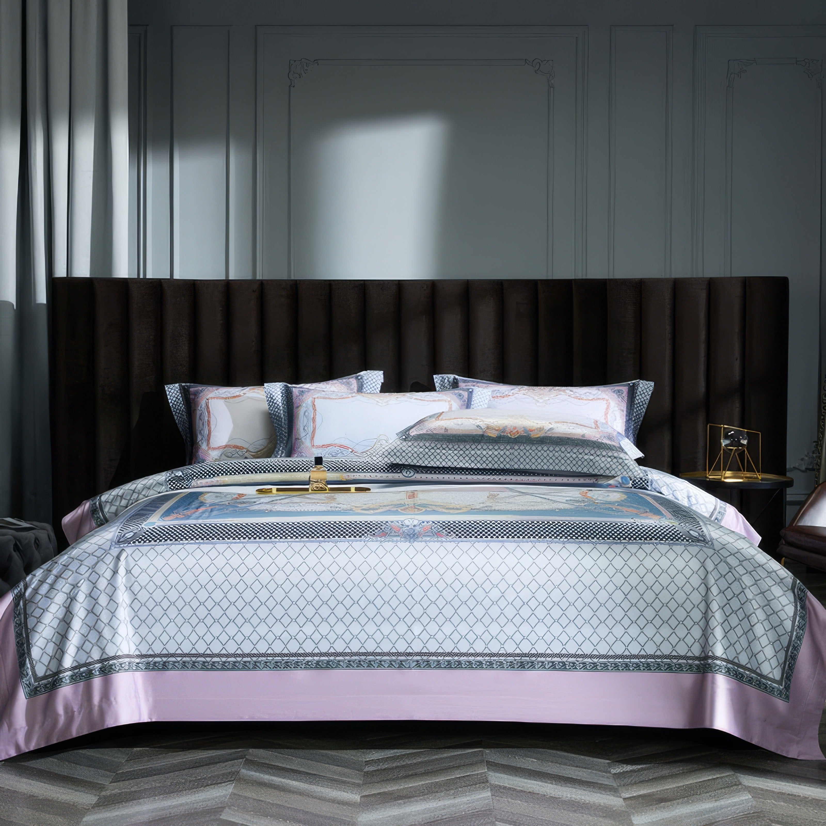 Luxurious bed with a white and gray geometric-patterned bedding set accented by soft pink borders. Matching pillowcases complement the design, and a dark, upholstered headboard contrasts elegantly against the light-colored walls. Natural light illuminates the serene bedroom space.

