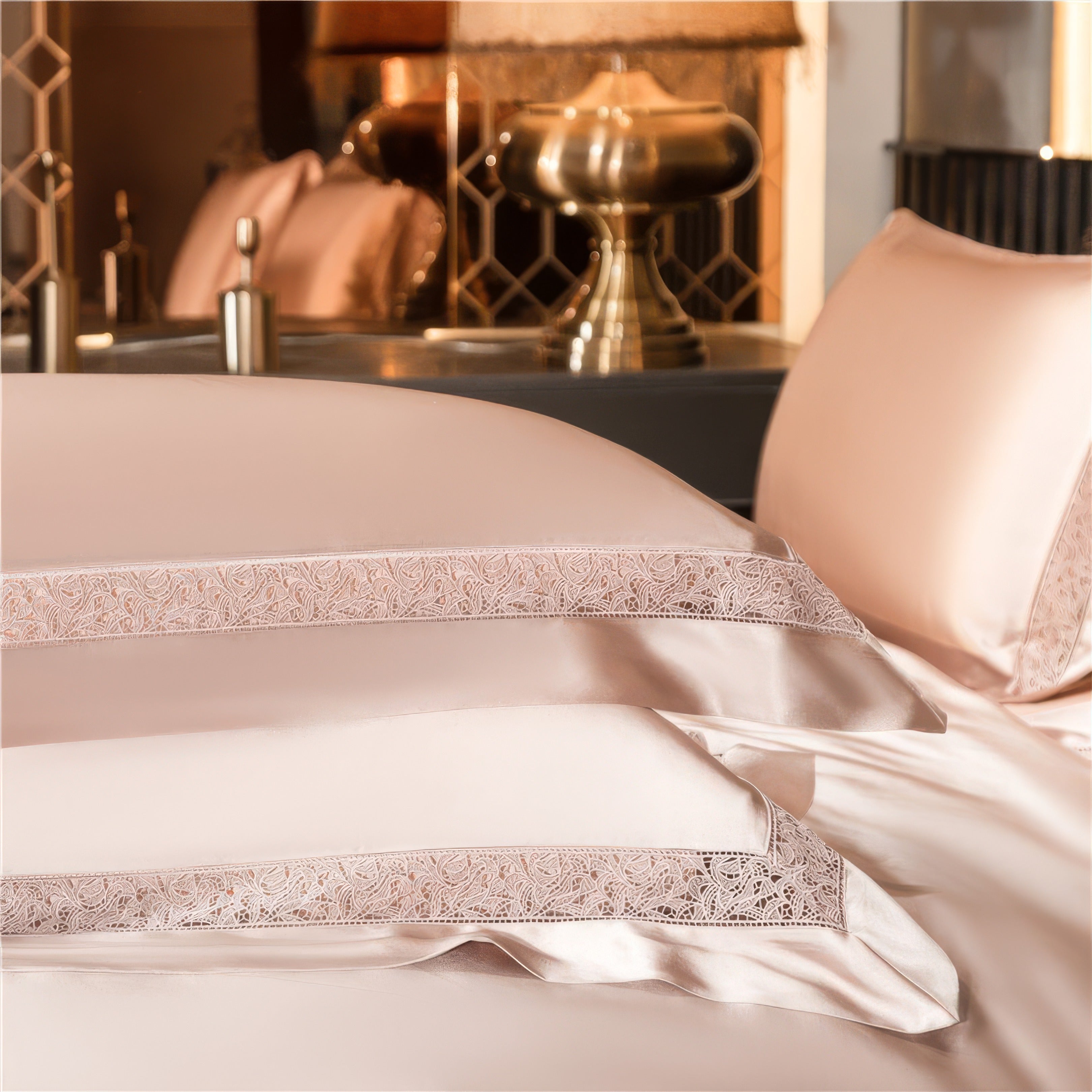 Close-up of a champagne satin bedding set, highlighting the delicate lace trim on the pillowcases and duvet. The soft sheen of the fabric complements the luxurious ambiance, enhanced by warm lighting and golden decor in the background.