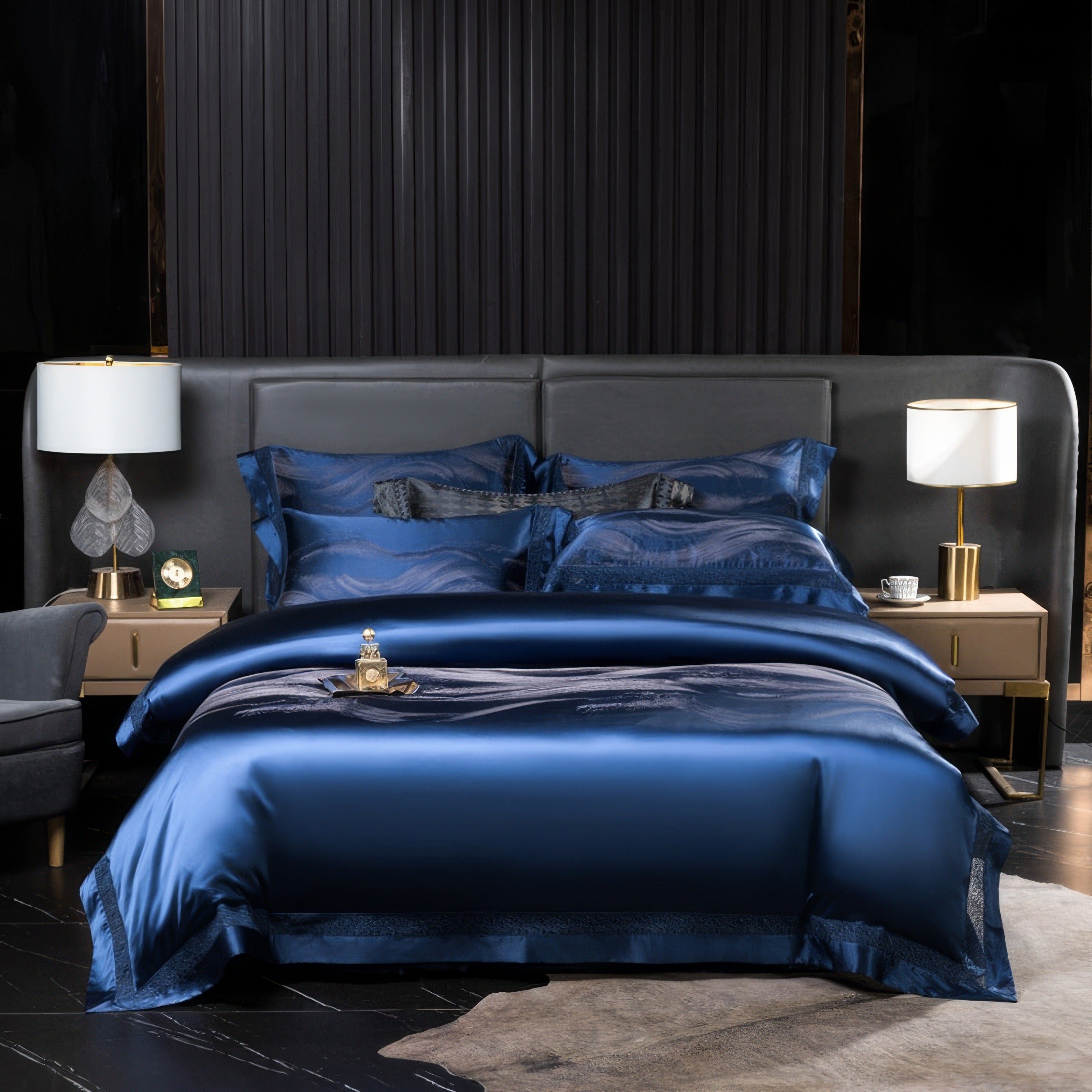 A sophisticated bedroom setting featuring a silky deep navy blue bedding set with a luxurious sheen. The bed is accented by matching pillowcases and shams, along with a subtle black design detail in the center of the pillows. Two sleek bedside tables hold contemporary lamps with white shades and golden bases, completing the elegant and modern aesthetic.

