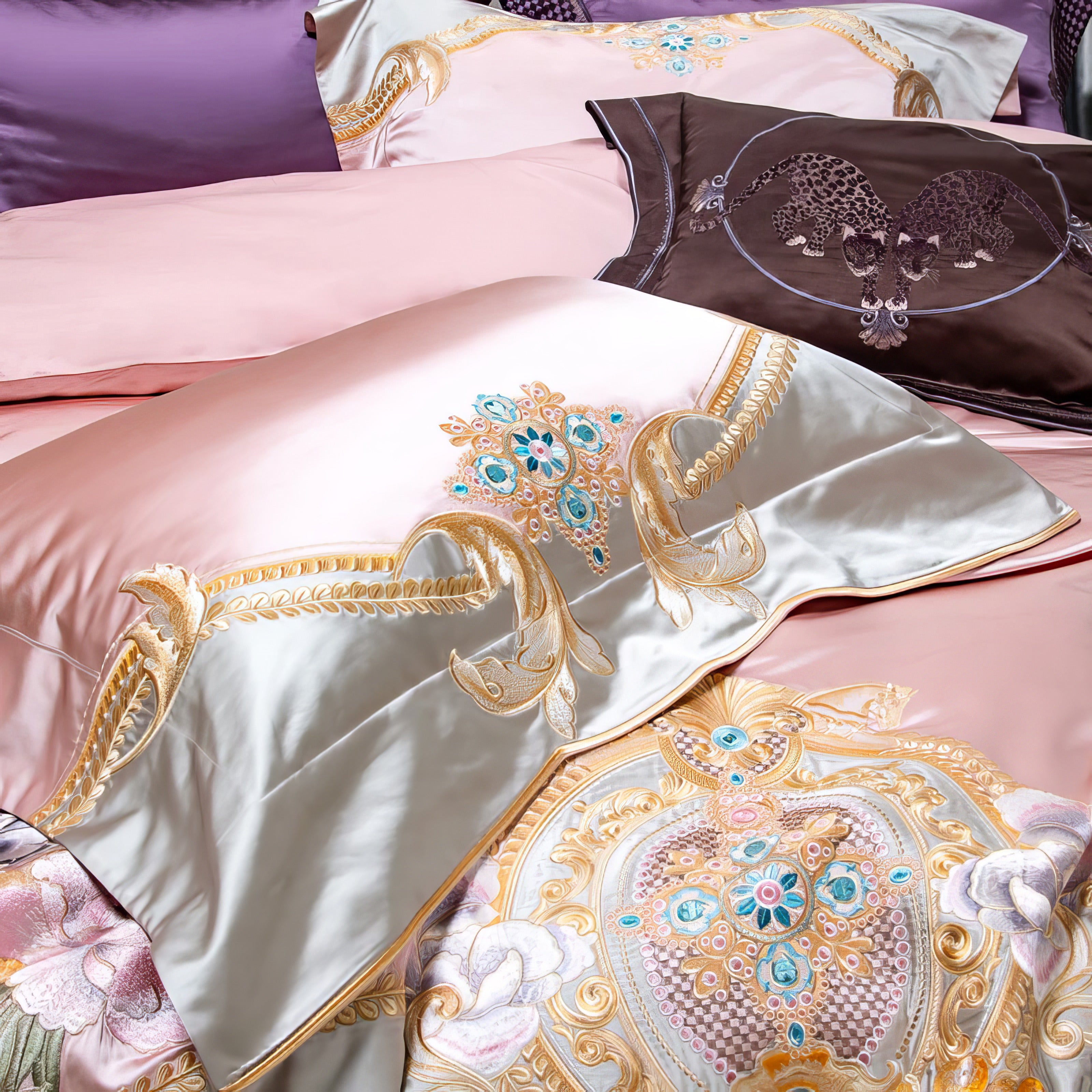 A close-up of an opulent bedding set featuring a pink and ivory base adorned with intricate gold embroidery and turquoise gemstone accents. The centerpiece pillow showcases lavish detailing with a majestic embroidered pattern, while the surrounding pillows include complementary blush and deep brown tones with elegant designs, exuding luxury and sophistication.