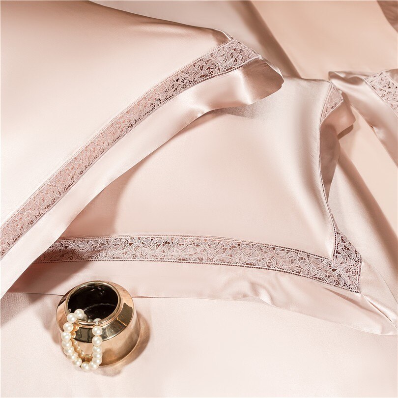 Close-up of champagne-colored satin pillowcases adorned with intricate lace trim along the edges, showcasing the luxurious texture and elegant craftsmanship. A small golden bowl with pearl accents adds a touch of sophistication to the scene.