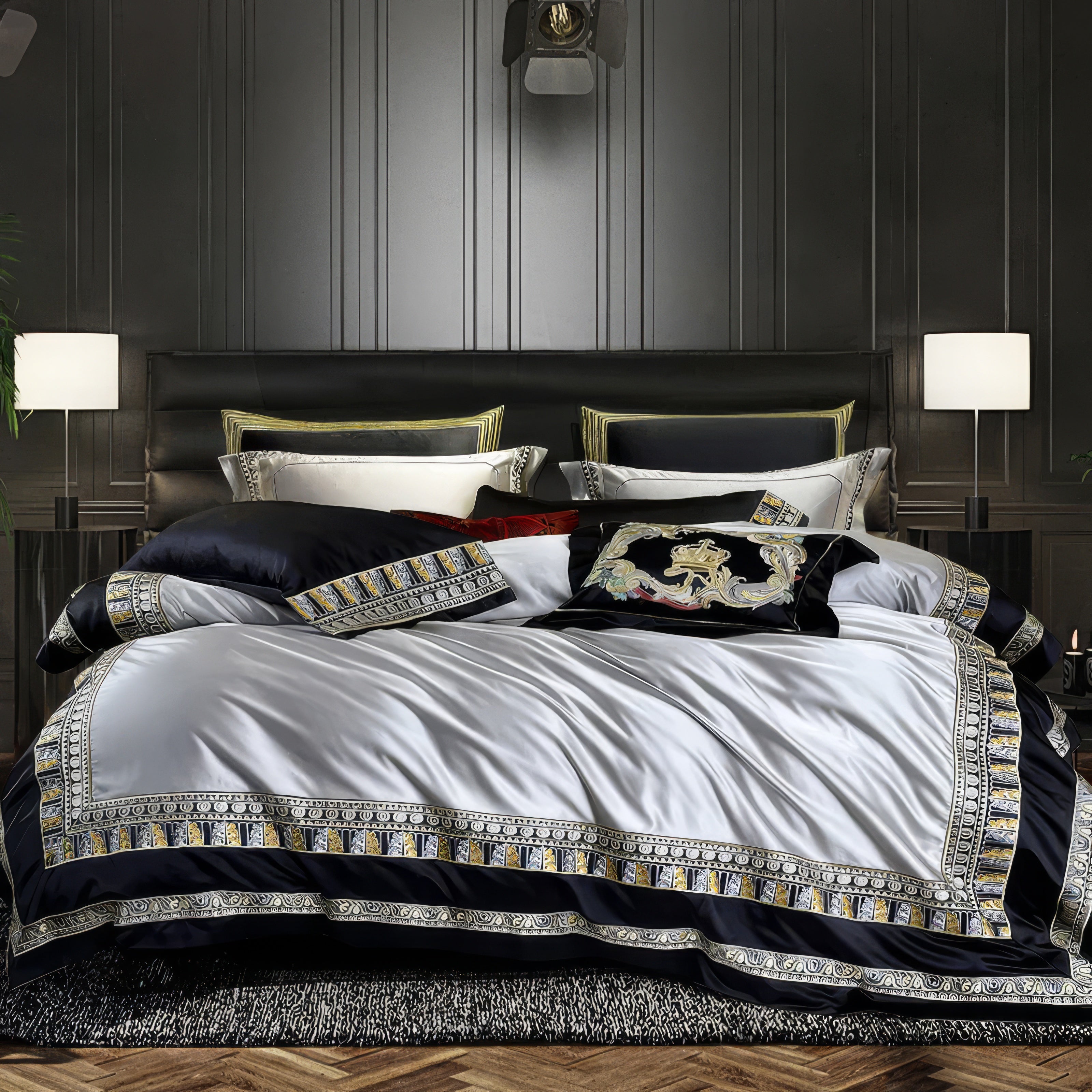 A luxurious bedding set in a sophisticated color palette of black, white, and gold, featuring an intricate geometric border design. The centerpiece is a velvet black throw pillow with ornate multicolored embroidery, including a regal gold crown motif. Complementing pillows in contrasting hues, including deep navy and white with decorative trims, enhance the layered look. 