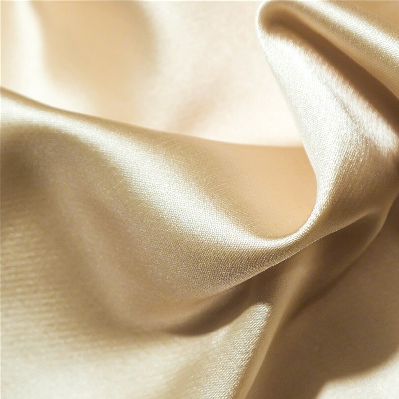 A close-up of luxurious cream-colored silk fabric, showcasing its smooth, glossy finish and fluid drape. The soft texture and natural sheen highlight the premium quality and elegance of the material.