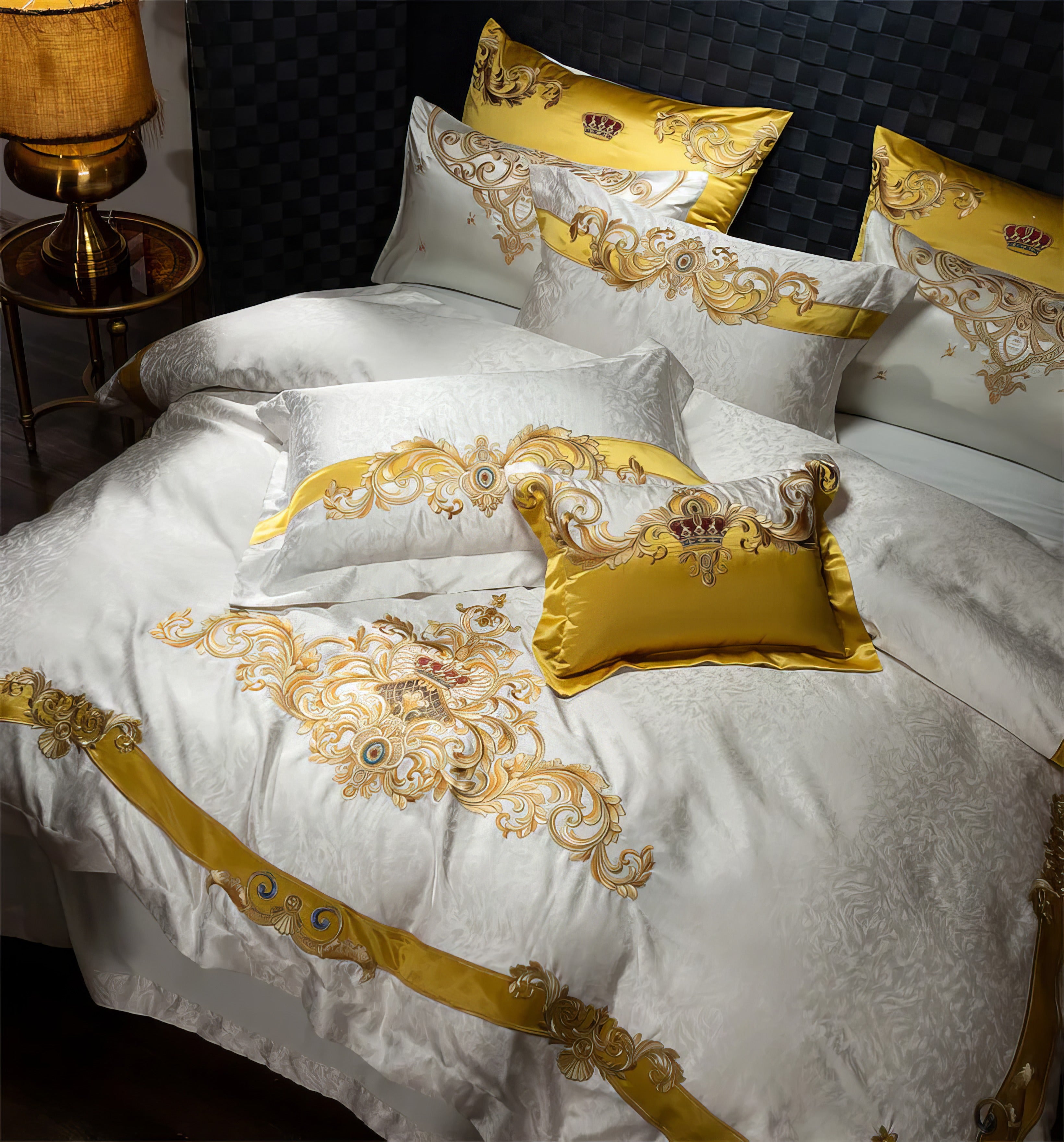 A luxurious bedding set showcasing intricate golden embroidery on a pristine white base. The design features regal crown motifs and ornate baroque patterns, accentuated with vibrant gold trims. Included are matching pillowcases and a golden decorative pillow, enhancing the grandeur. The textured duvet adds depth, while a warm lamp on a brass side table completes the elegant ambiance. Perfect for a majestic and opulent bedroom setting.