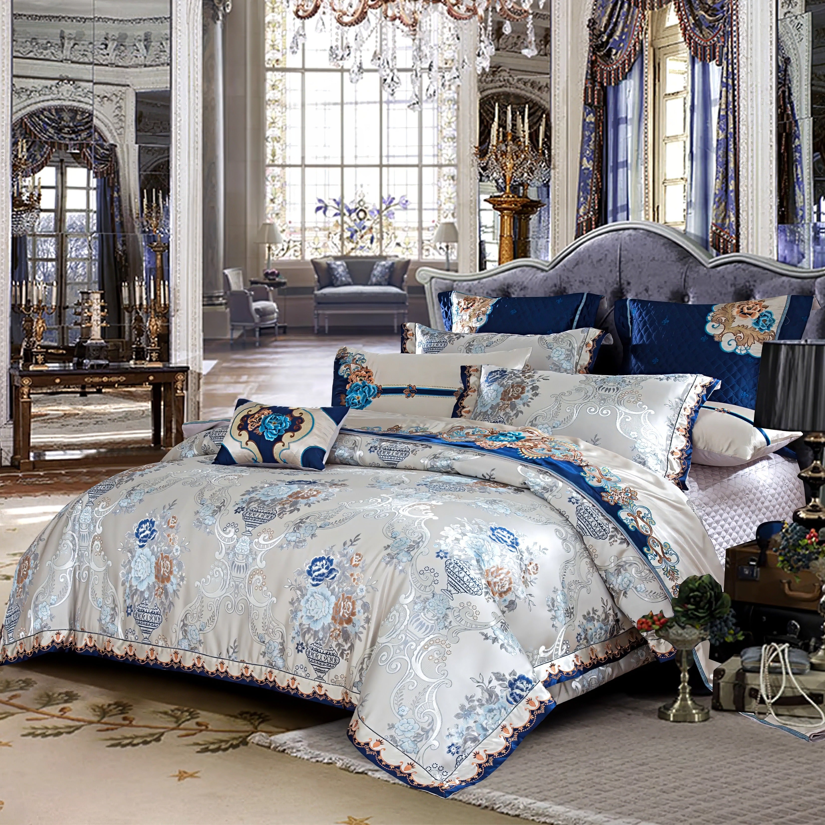 A palatial bedroom with a grand and lavish ambiance, featuring a plush, tufted velvet headboard in a regal shade of deep blue. The luxurious bedding is adorned with an intricate floral design in hues of blue, gold, and cream, enriched by decorative pillows and quilted accents. The background reveals a spacious room with ornate chandeliers, tall mirrors, and expansive windows dressed in heavy drapes, offering a glimpse of classical elegance and timeless luxury. 