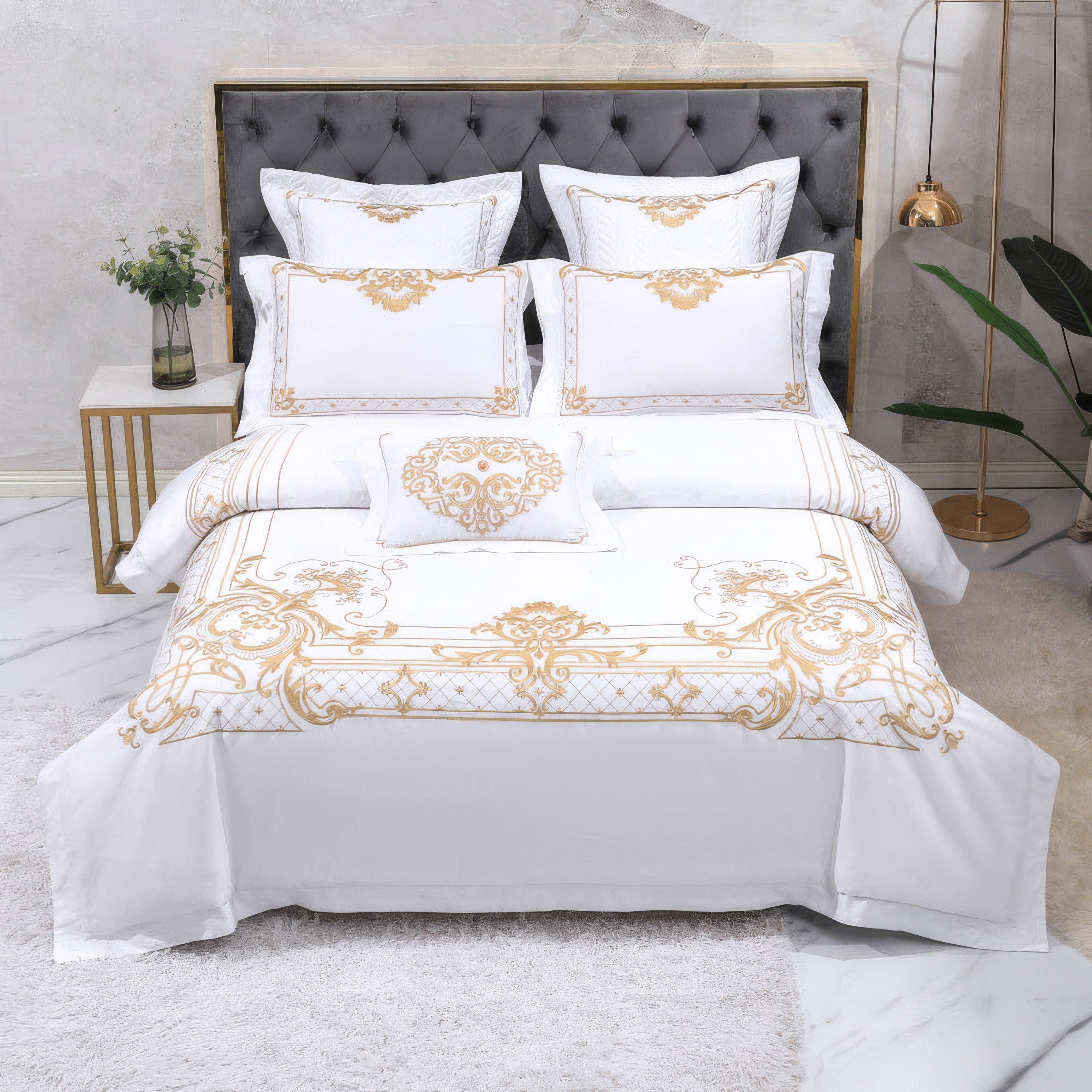 A luxurious white bedding set adorned with intricate gold embroidery, creating a regal and sophisticated appearance. The set features a tufted gray headboard, elegantly framed by a modern gold-accented bedside table and lamp. Plush pillows and cushions add layers of comfort and opulence, while the marble floor and soft area rug complete the refined and polished bedroom design.