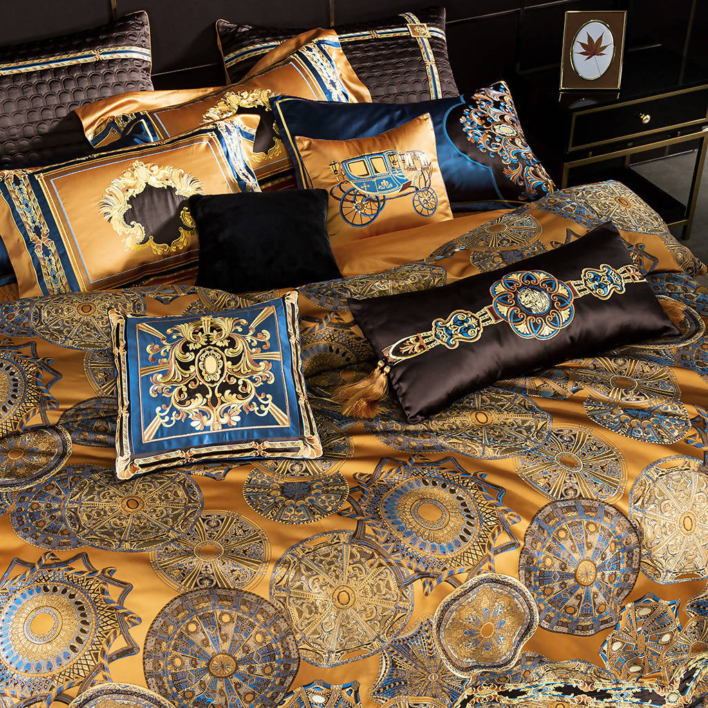 Close-up of an opulent bedding set featuring gold, blue, and black tones with intricate circular medallion patterns, ornate pillow designs, and a black velvet cushion accent.

